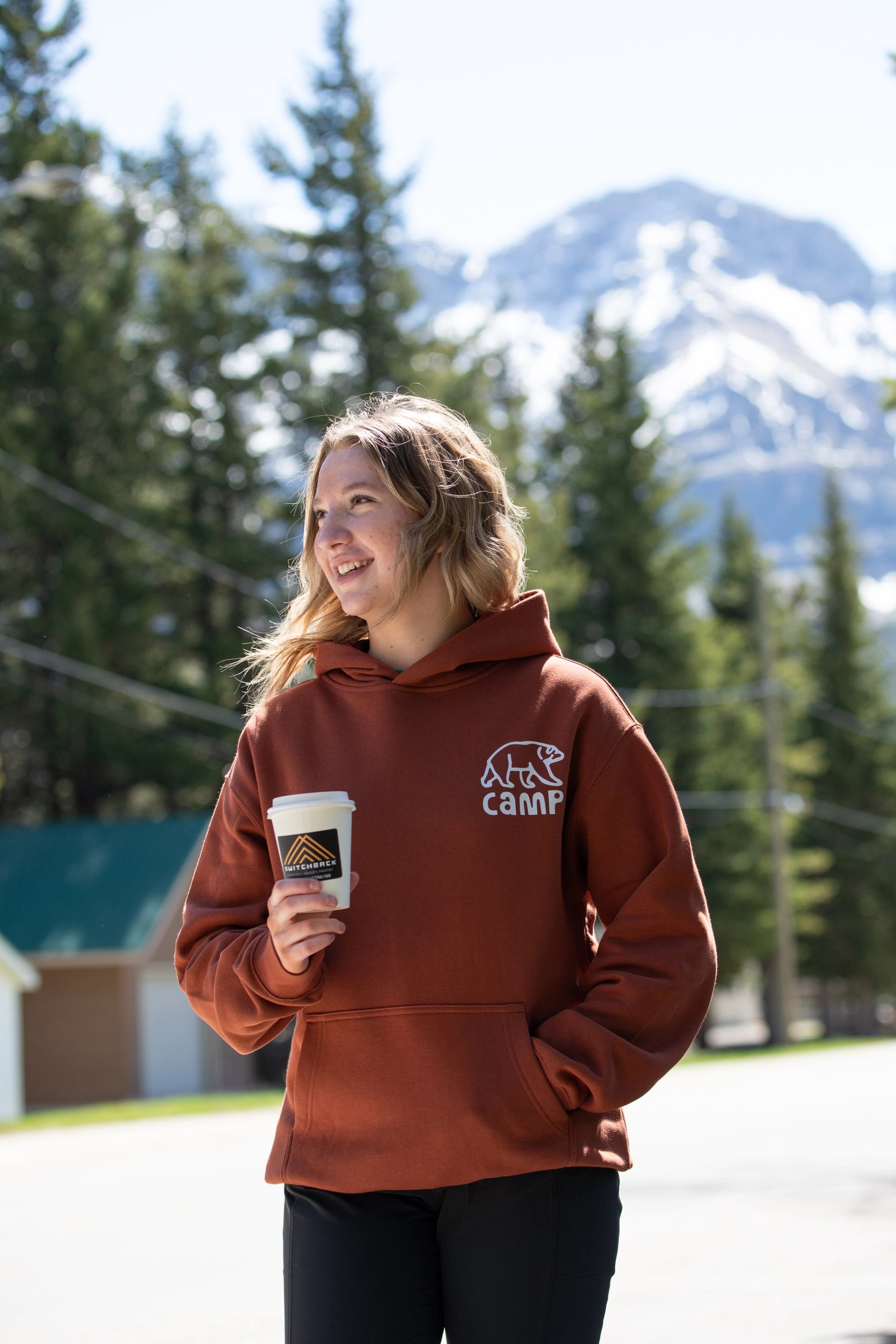 Person holding a Switchback Micro‑Cafe take‑away coffee with trees and a mountain in the background.