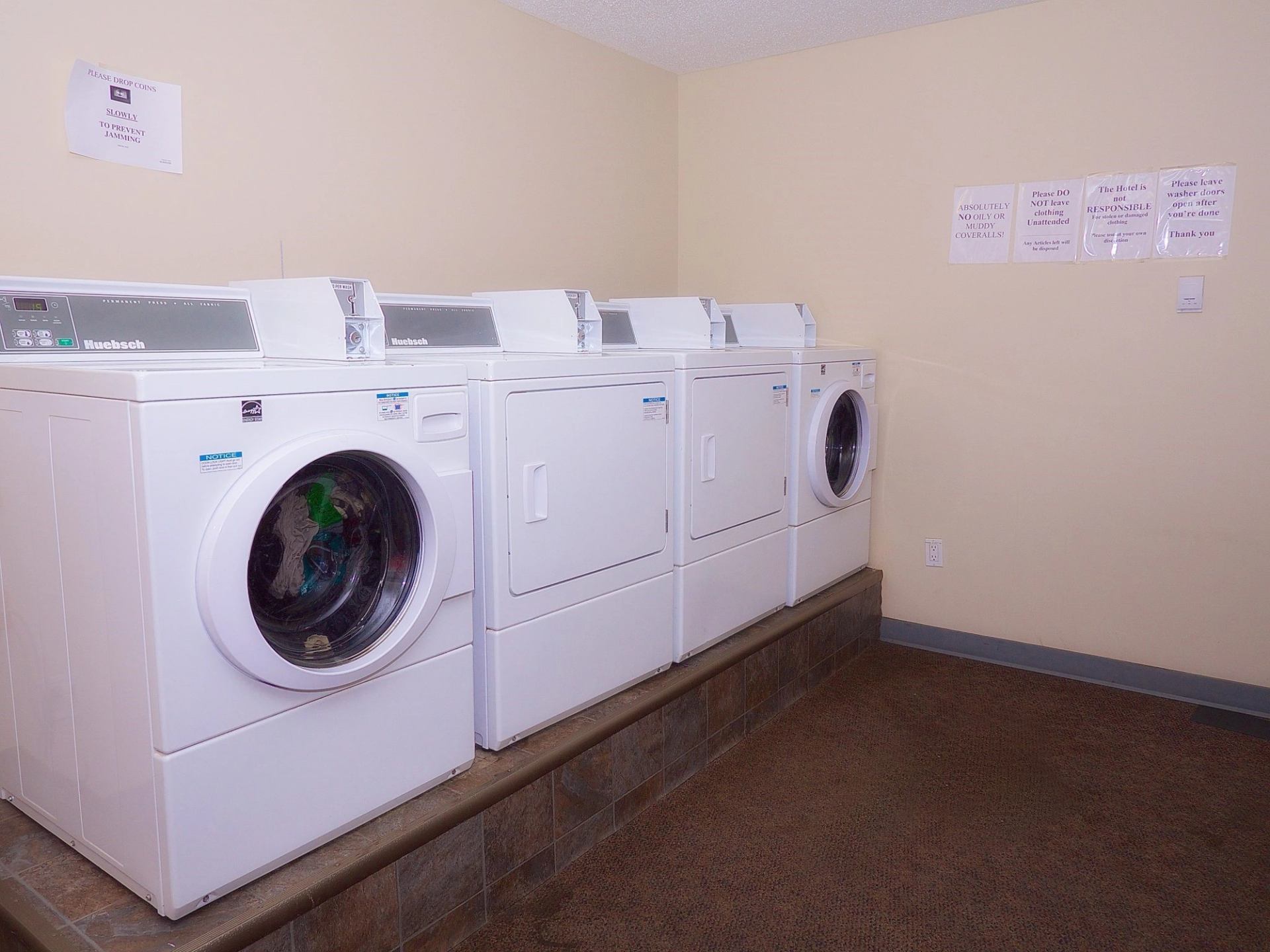 Laundry room with front-loading washers and dryers lined up under wall signs.