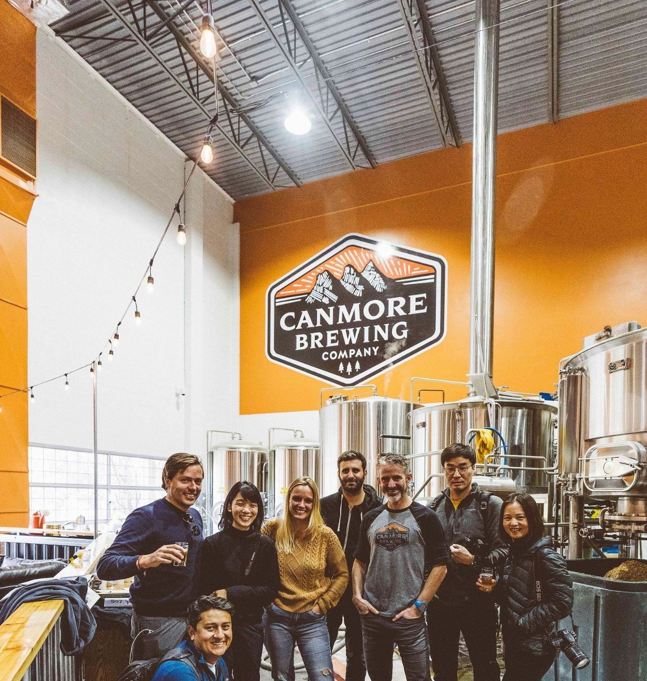 Group posing inside Canmore Brewing Company with stainless tanks.