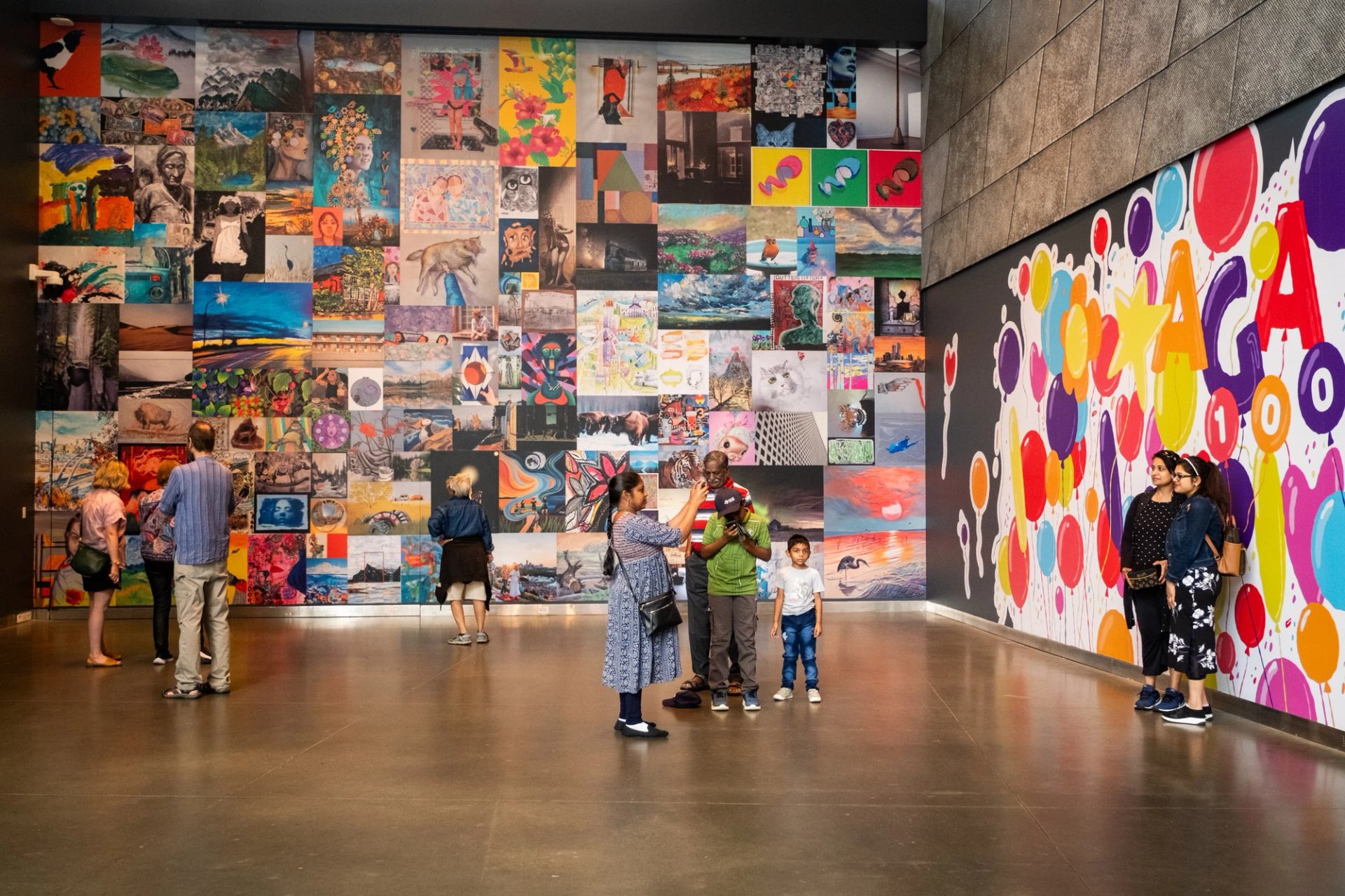 Visitors view colourful artwork covering two walls in a spacious gallery.
