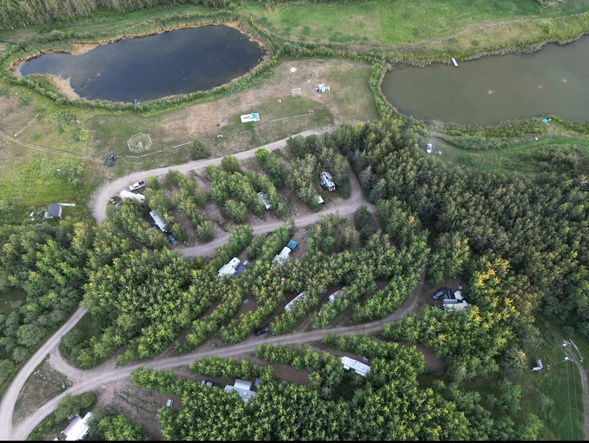 Aerial view shows RV sites nestled among trees beside two ponds connected by winding gravel roads.
