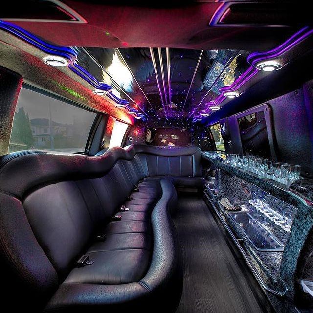 Quest Limos interior with black leather seats, LED lighting, and bar area with glassware.