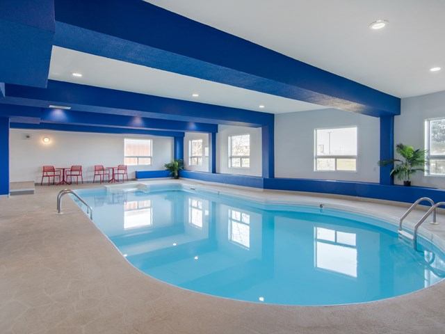 Indoor swimming pool with blue accents, lounge chairs, and windows at Comfort Inn & Suites.
