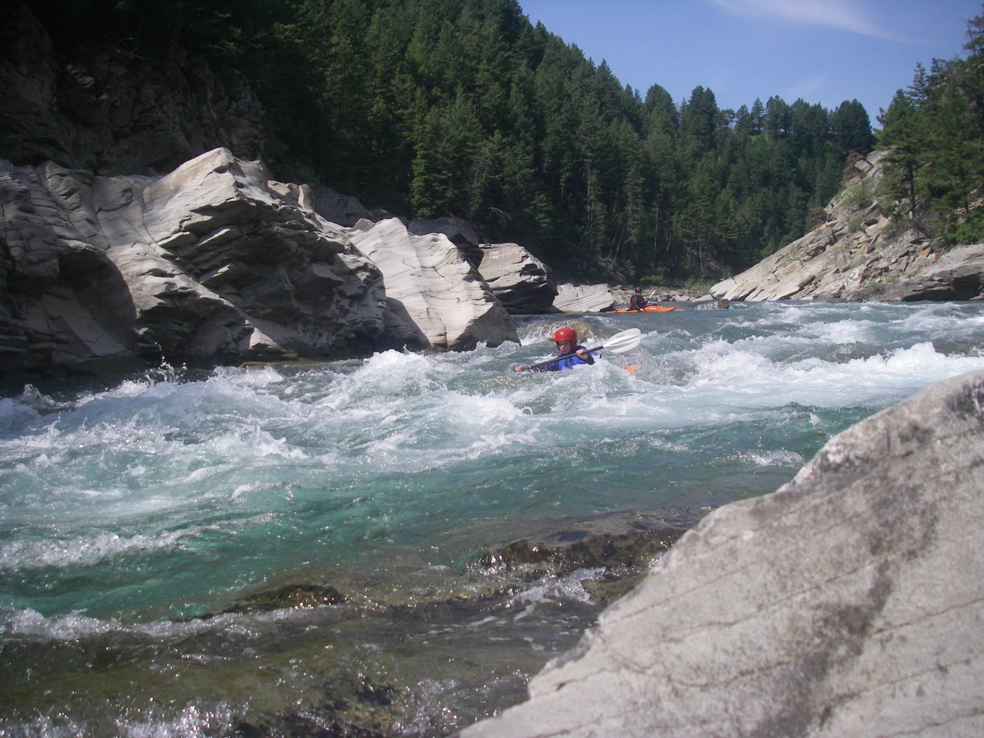 Kayaker moving through fast whitewater in a rocky river canyon.