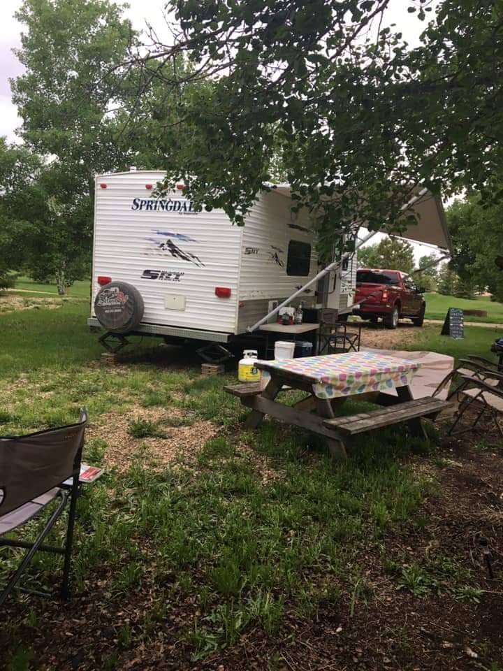 RV campsite with picnic table, red car, and shaded trees.