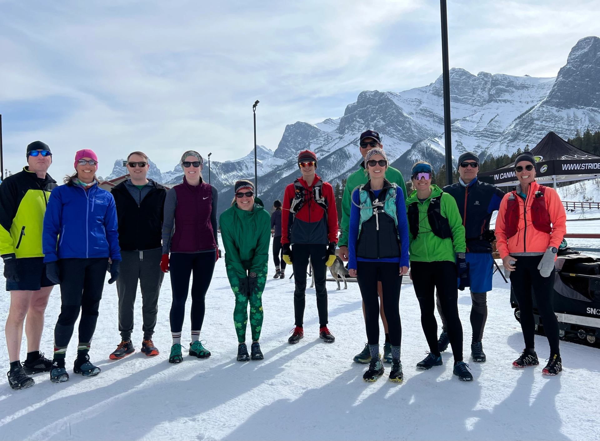 Group of winter runners standing on snow with mountains and lodge in the background.