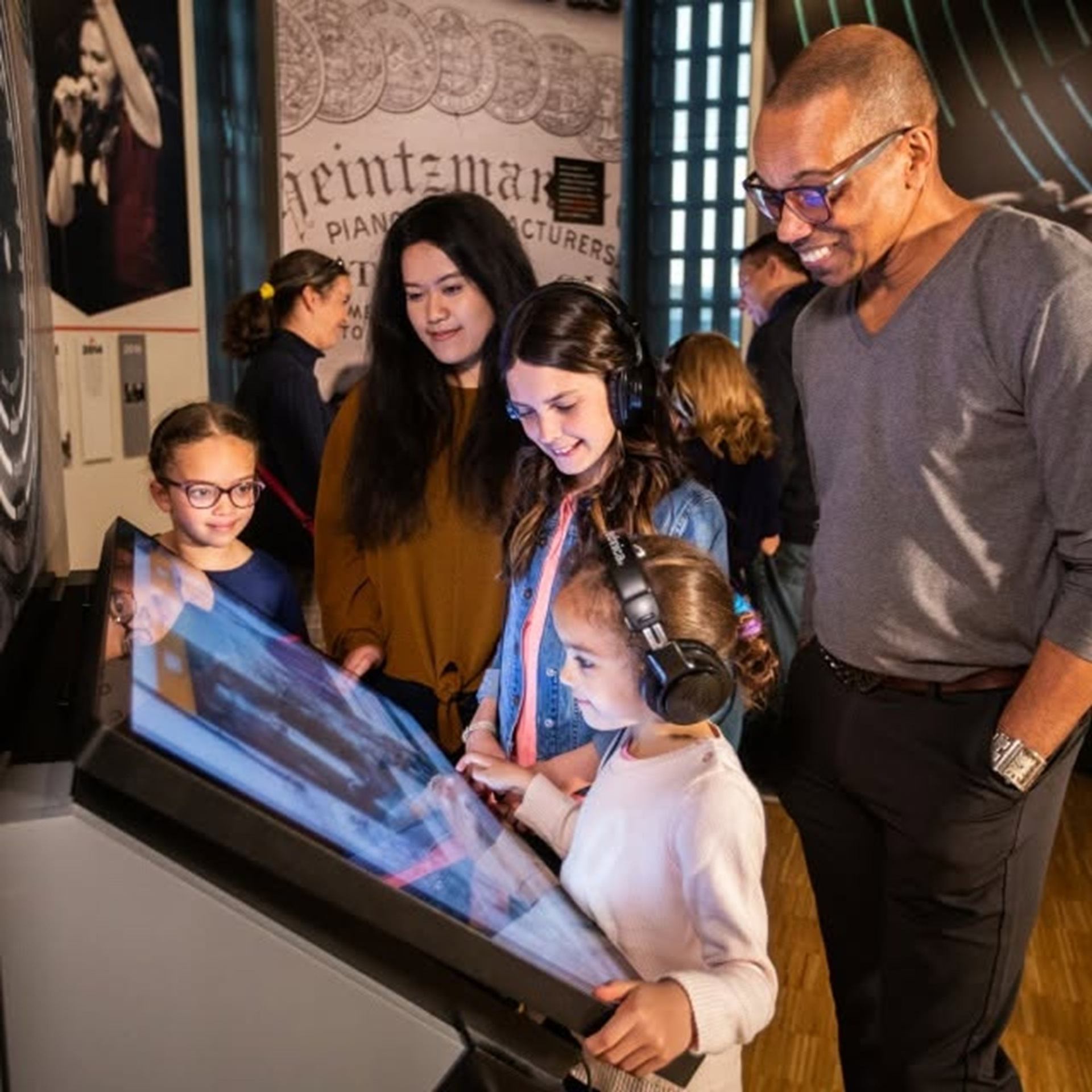 Children wearing headphones use an interactive touchscreen as adults watch.