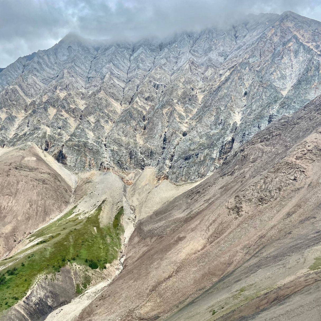 Rocky mountain ridge above scree slopes and green valley under low clouds.