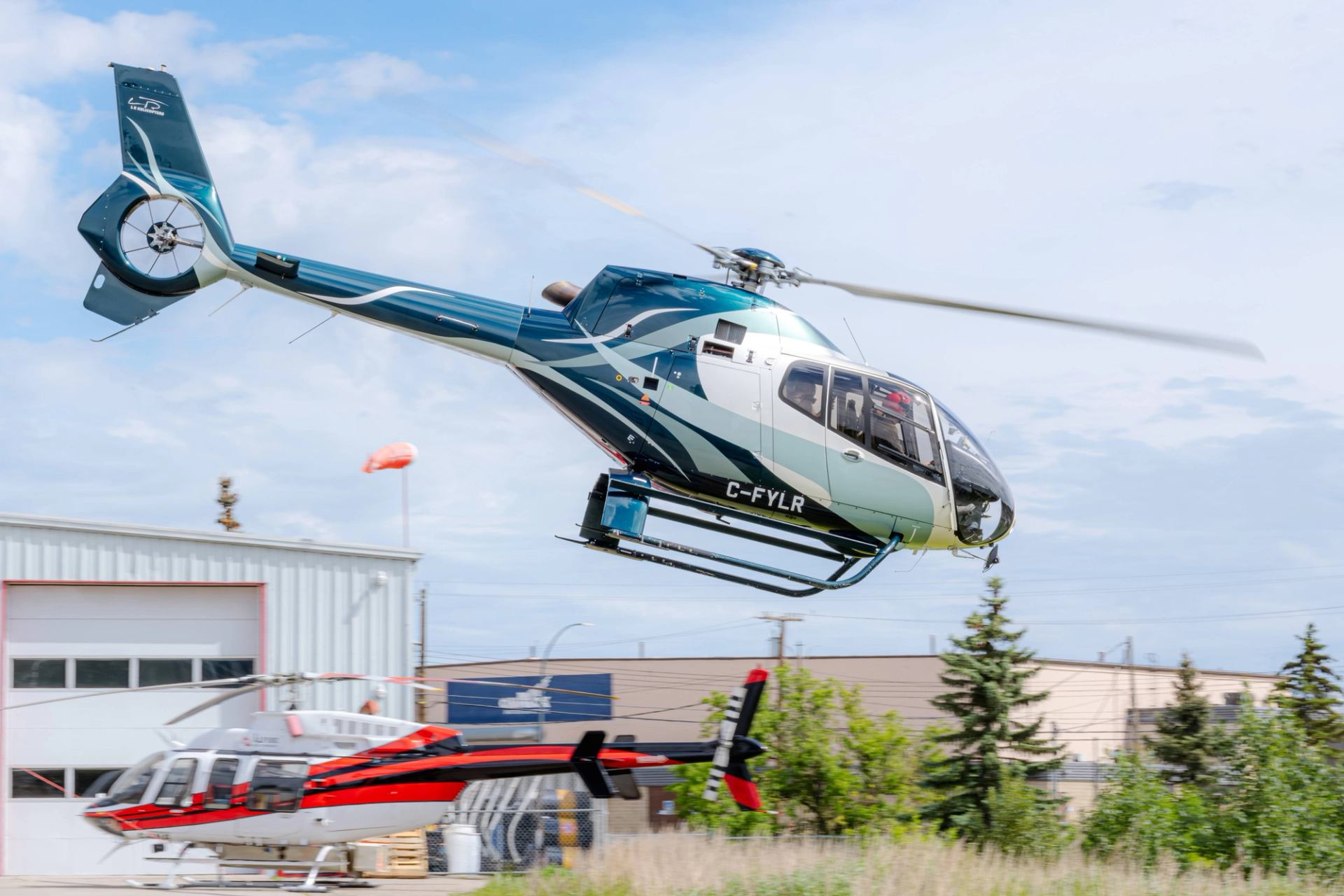 Helicopter flying above hangar building with rotor in motion, Calgary airport area.