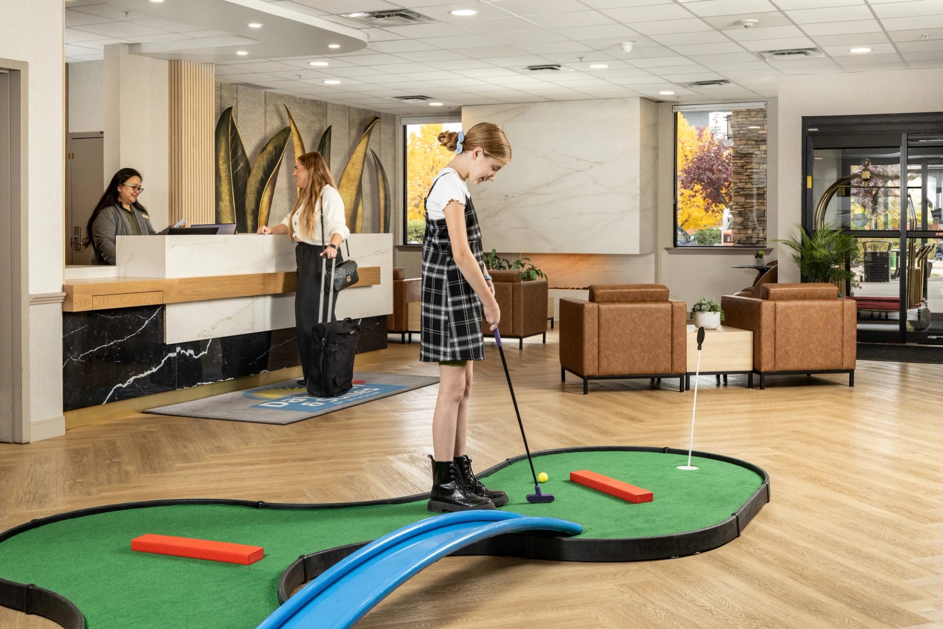Bright lobby, with seating area, white marble fireplace, front desk and a mini golf area