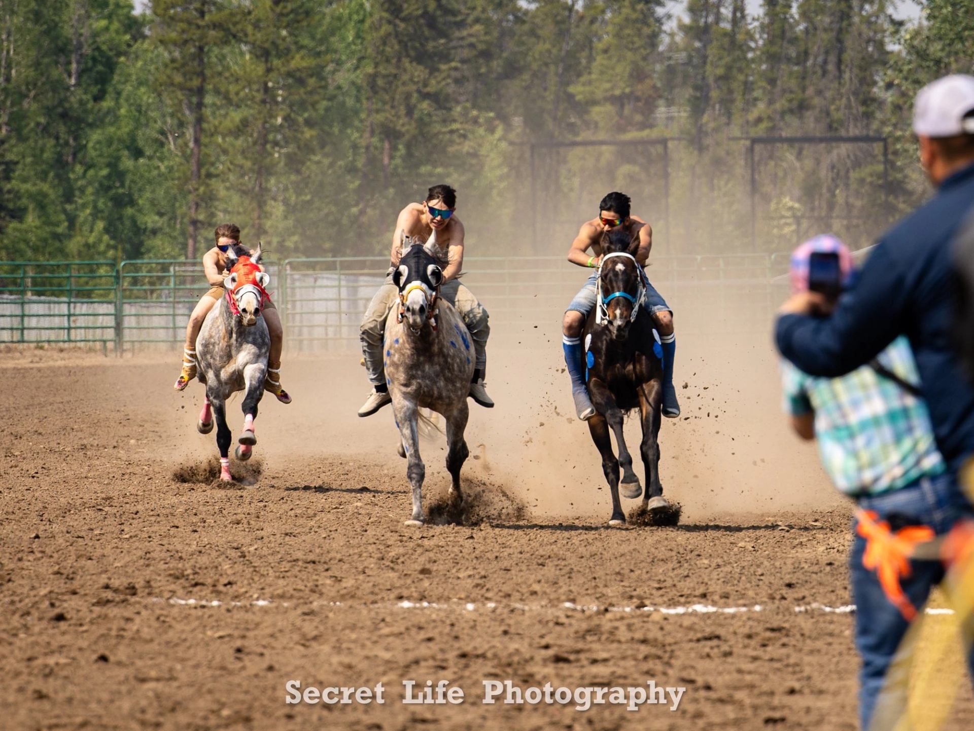 Riders racing horses across a dusty arena during a cultural event.