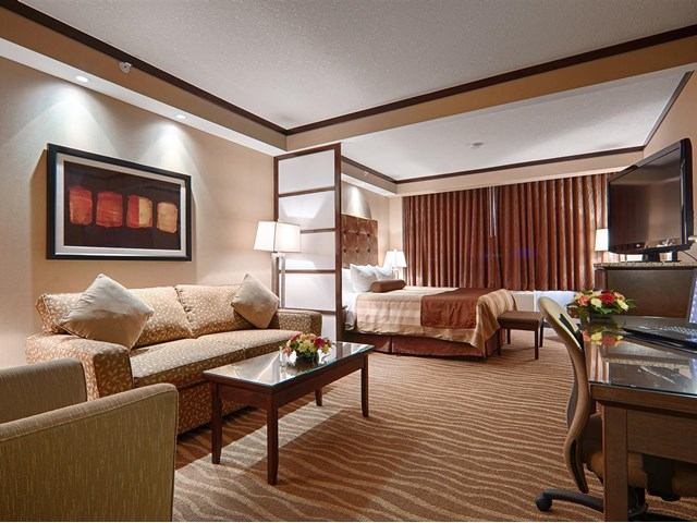 Elegant hotel room with seating area, bed, warm lighting, and modern decor.