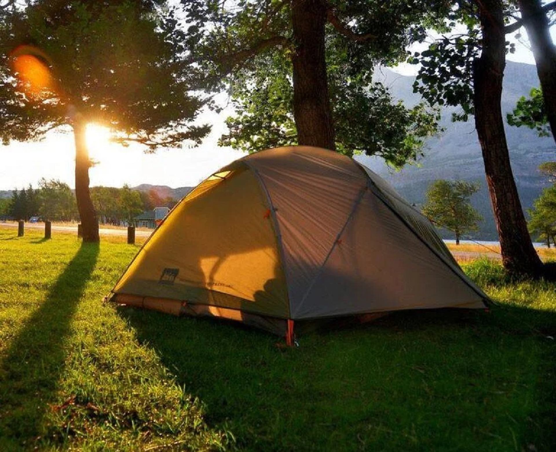 A camping tent on green grass glowing in the warm light of a sunset.
