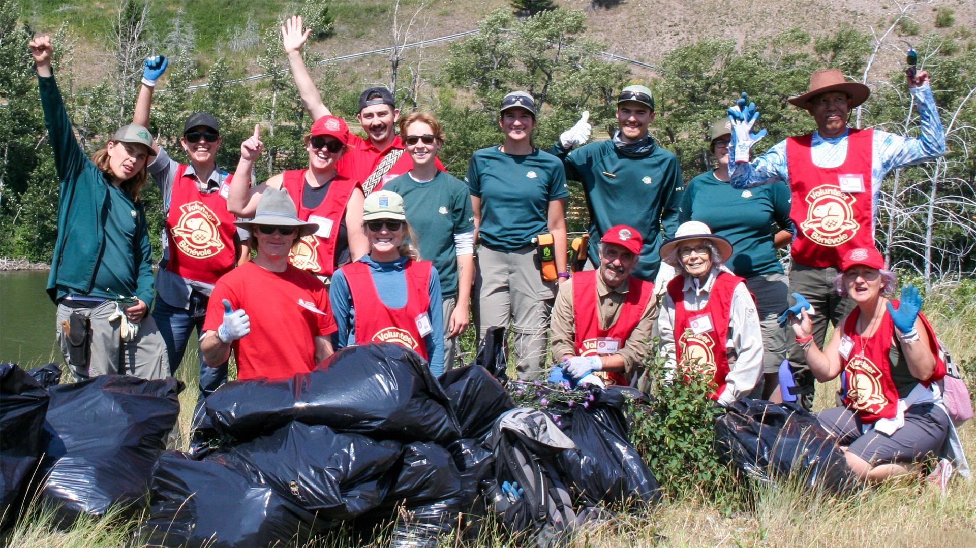 A group of volunteers pose with several black garbage bags filled with knapweed