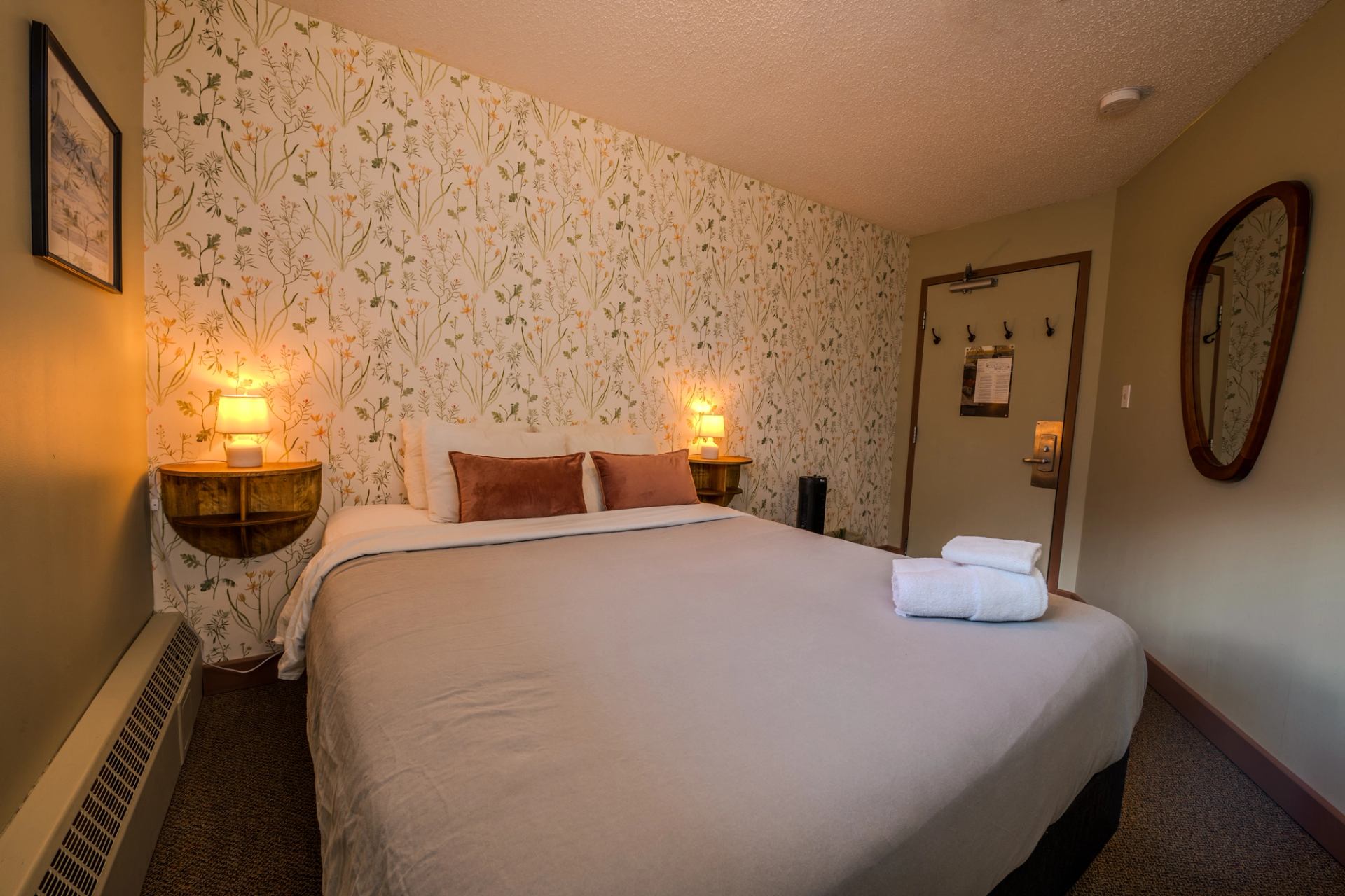 Cozy bedroom with a queen bed, warm lighting, and floral accent wall at HI Banff Alpine Centre.