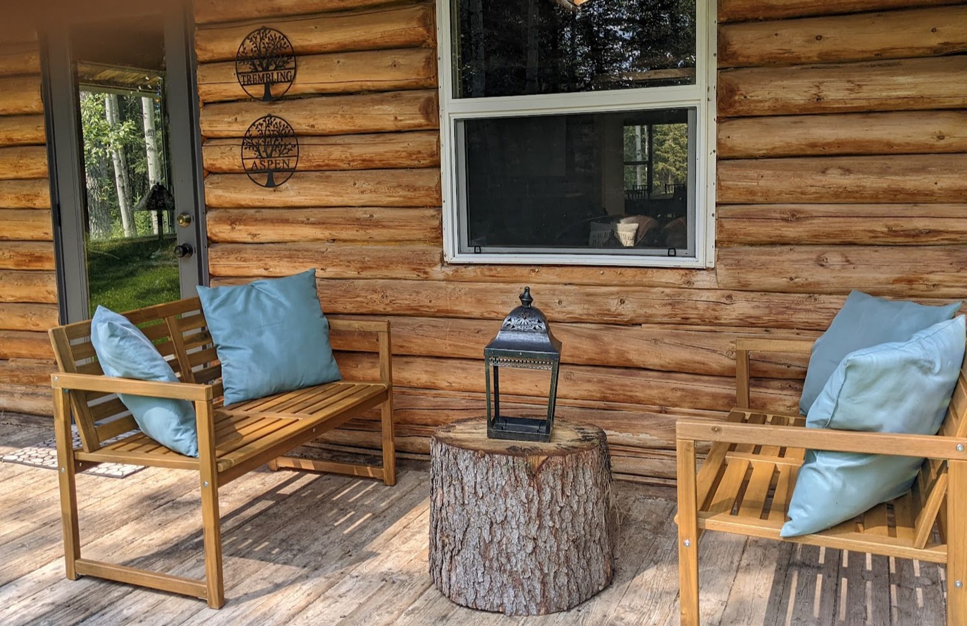 Wooden porch with chairs and cushions outside a log cabin at Trembling Aspen Retreat.
