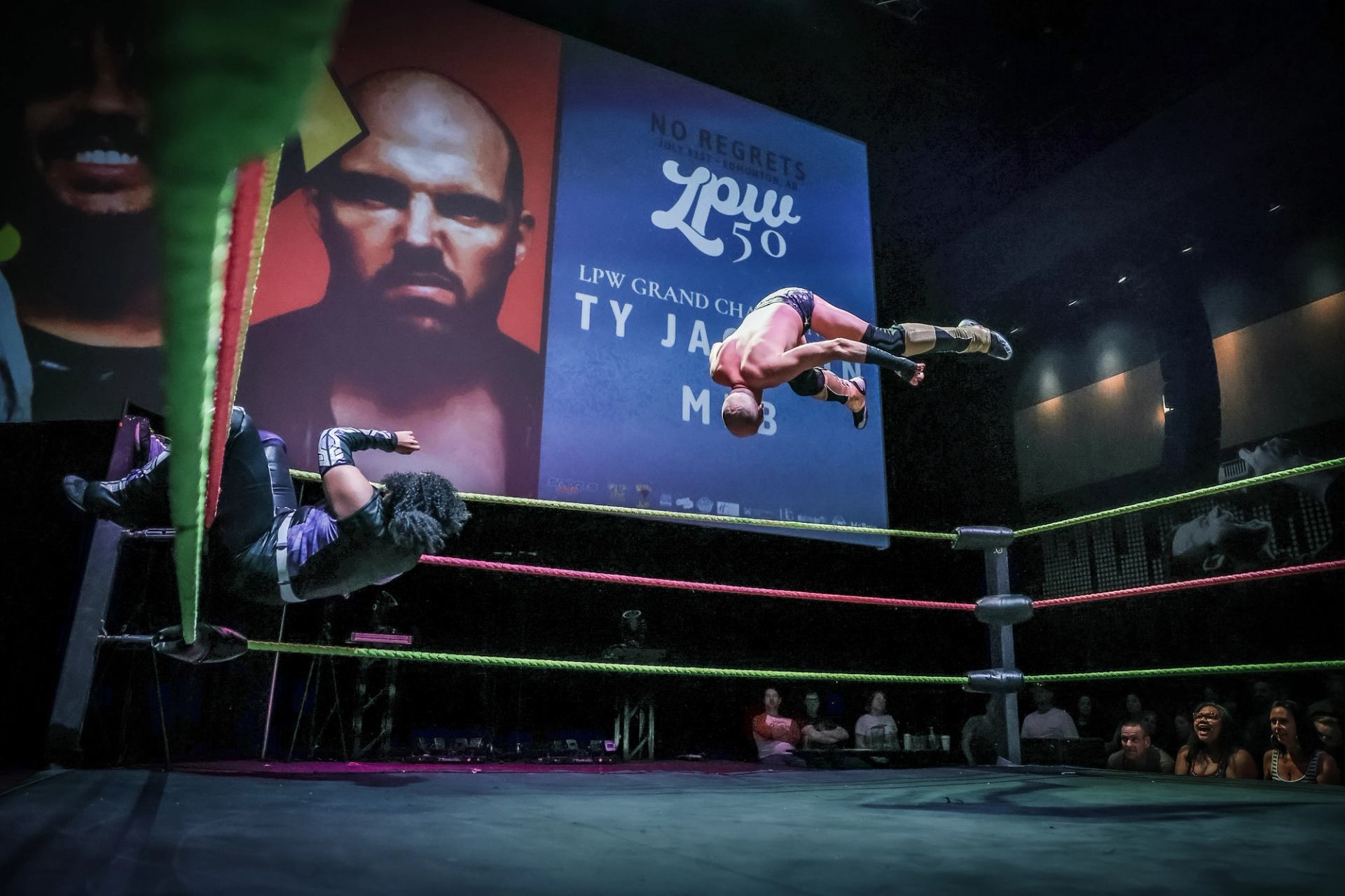Wrestler flips through the air toward an opponent in a brightly lit ring.