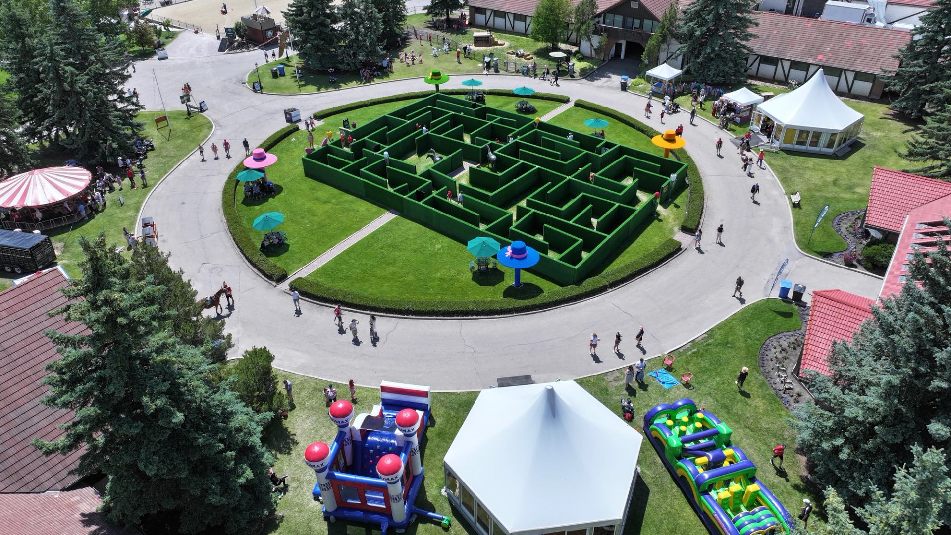 Aerial view of outdoor hedge maze surrounded by paths, tents, rides and visitors.