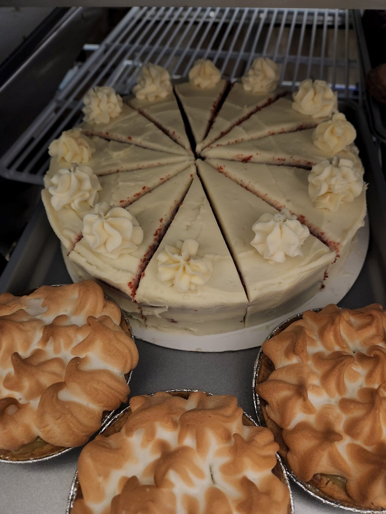 Decorated round cake with whipped cream flowers, surrounded by individual pastries in trays.