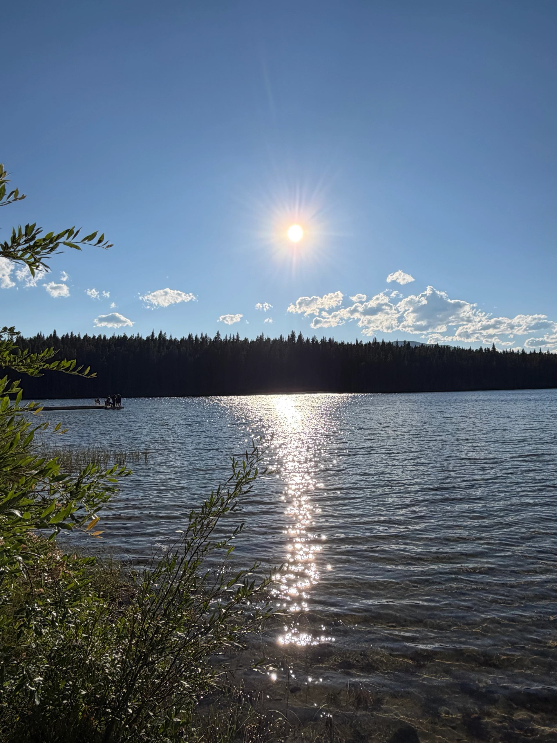 Sun reflecting on calm lake water with distant treeline and small dock.