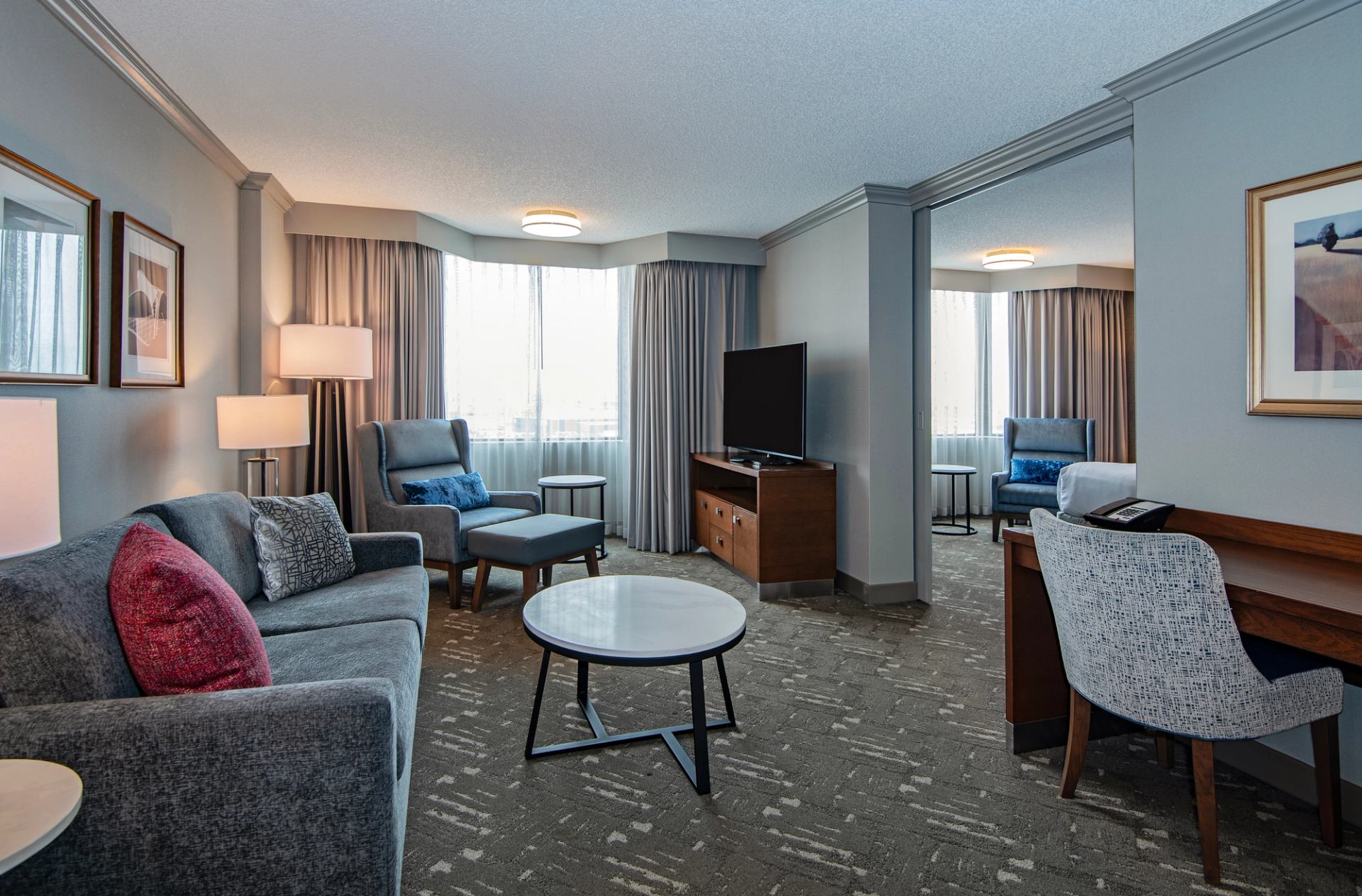 Hotel suite living area with sofa, armchairs, TV, coffee table and work desk.