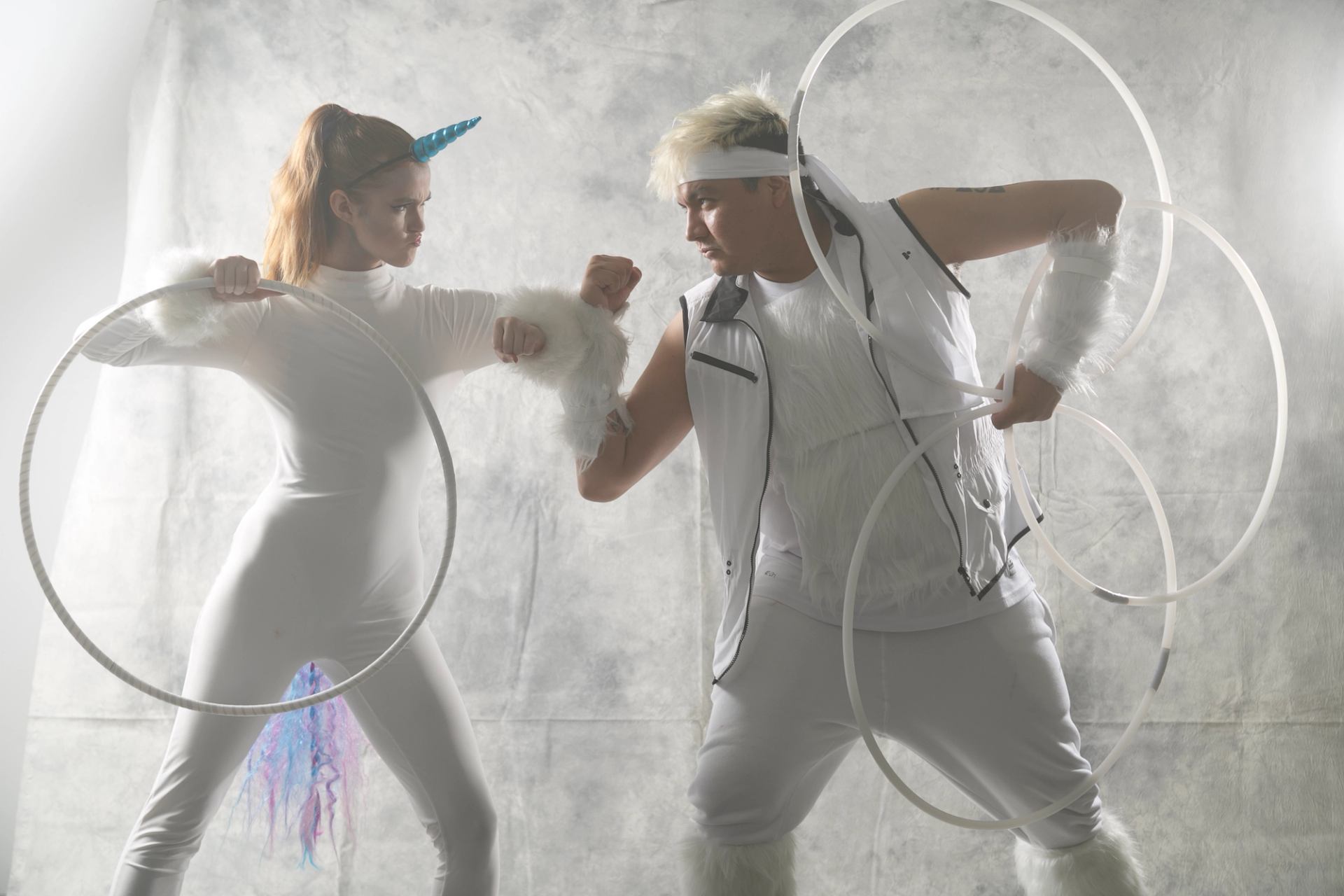 Two performers in white costumes pose with hoops against a light studio backdrop.