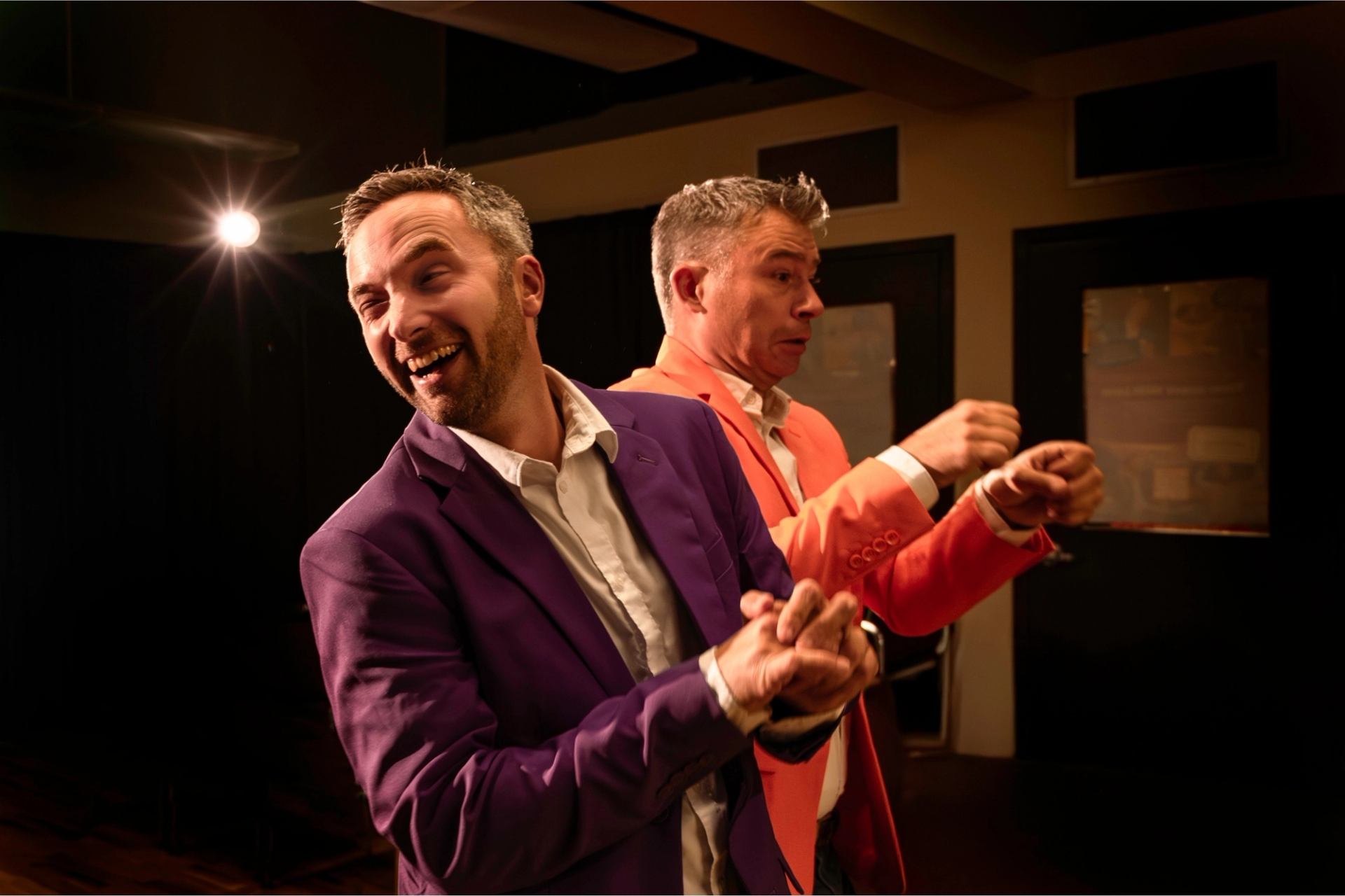 Two performers onstage in bright suits acting in a lively theatre scene