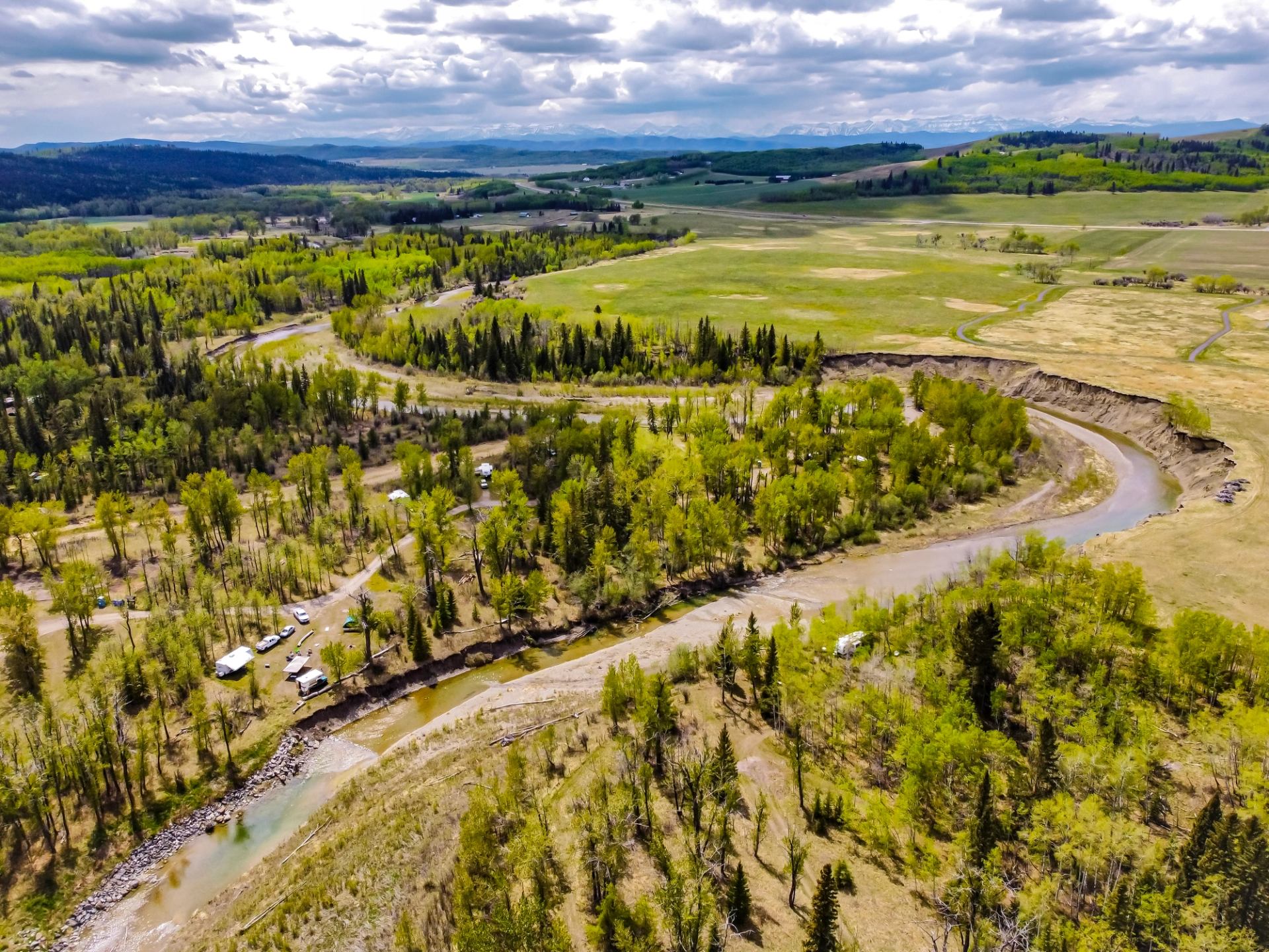 Aerial view of a winding river, trees, and open fields surrounding the Millarville Racing & Agricultural Society Campground.