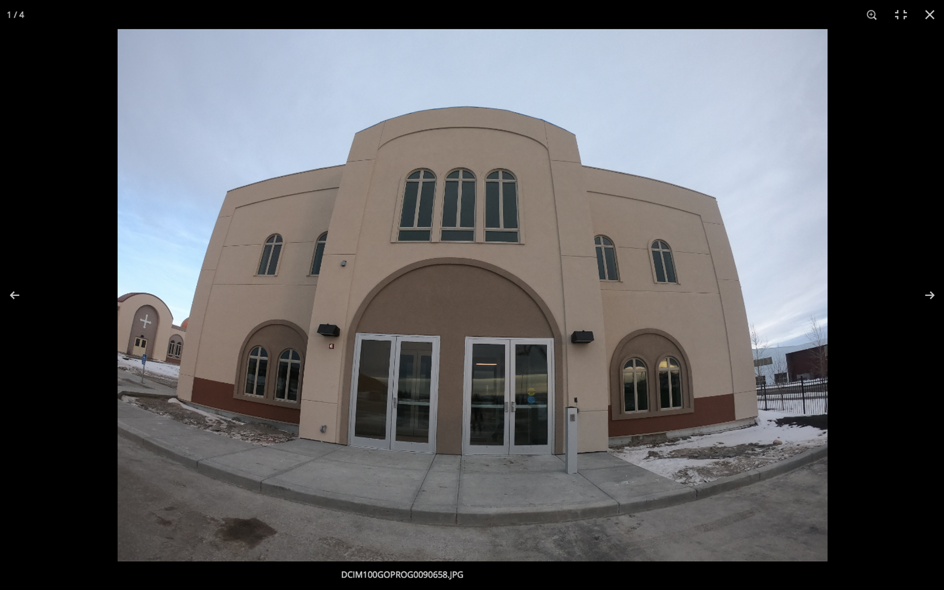 Front entrance of a beige building with arched doorway and four windows, under a cloudy sky.