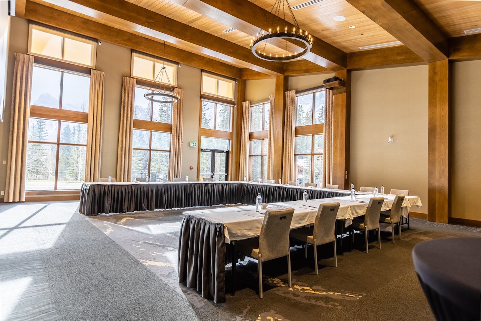 Large room with tall windows, U‑shaped tables, and mountain views outside