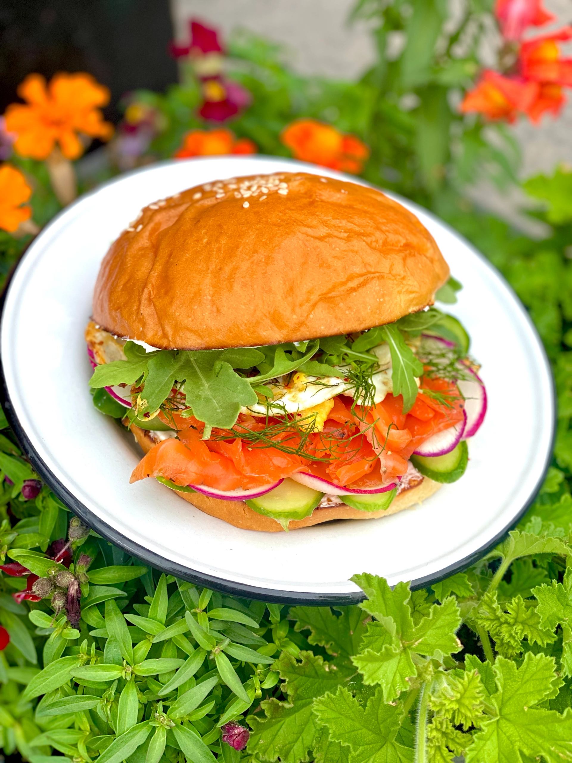 Gourmet sandwich with veggies and smoked salmon on a sesame bun.