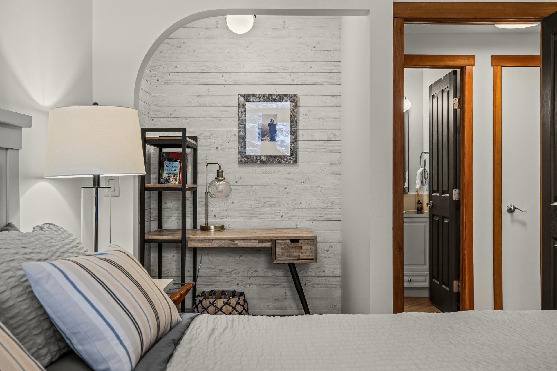 Bedroom with striped pillows, small desk and shelf, and doorway to bathroom.