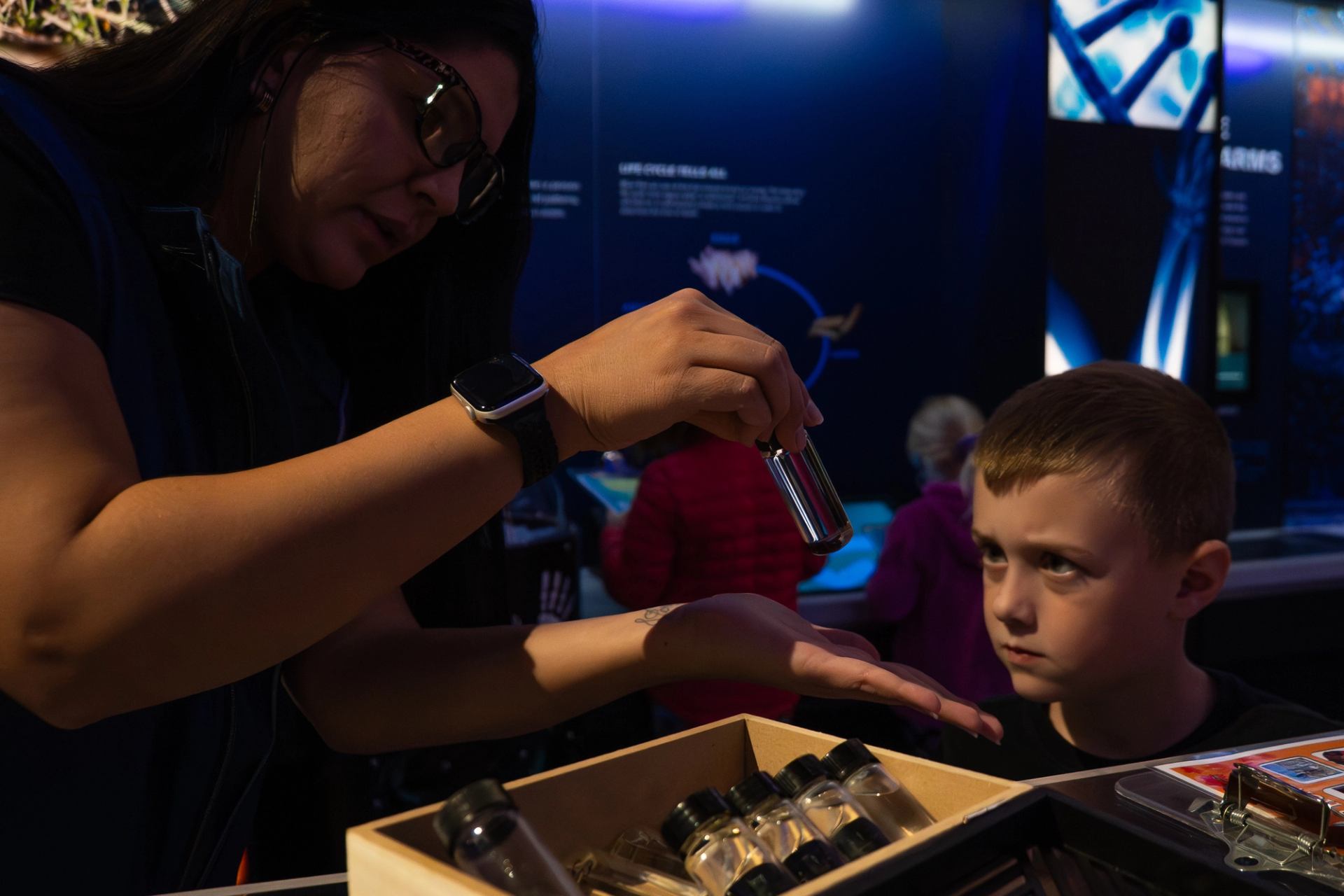 Person demonstrating a small vial at a science exhibit table with display cases nearby