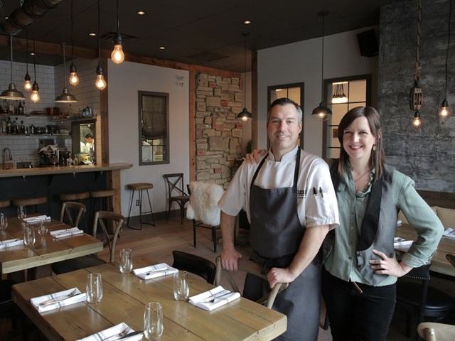 Two people in a cozy, rustic restaurant with set tables.