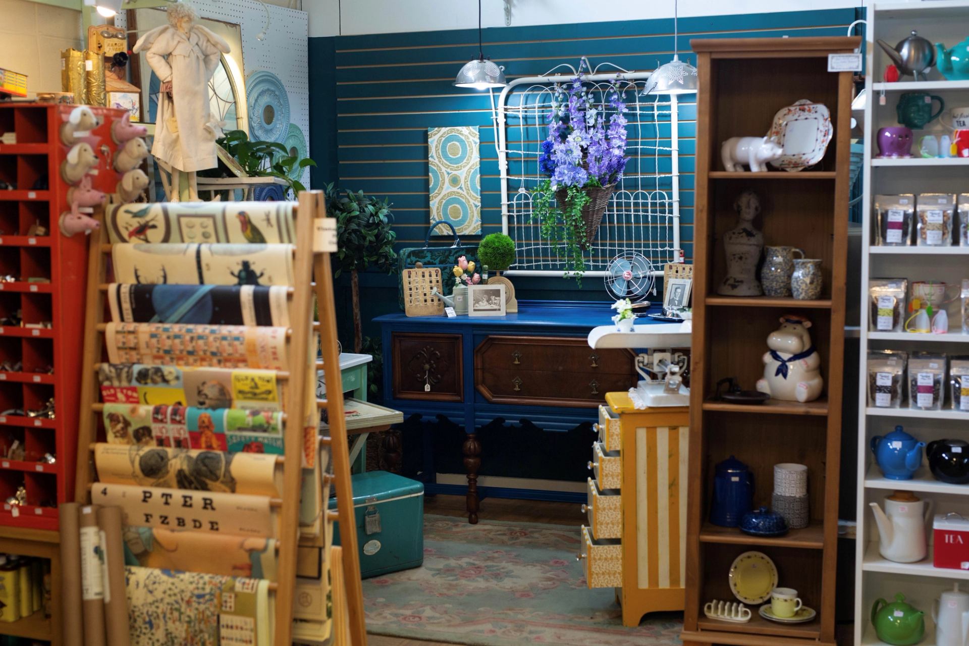 Antique shop display with shelves, patterned fabrics, blue dresser, and assorted ceramics.