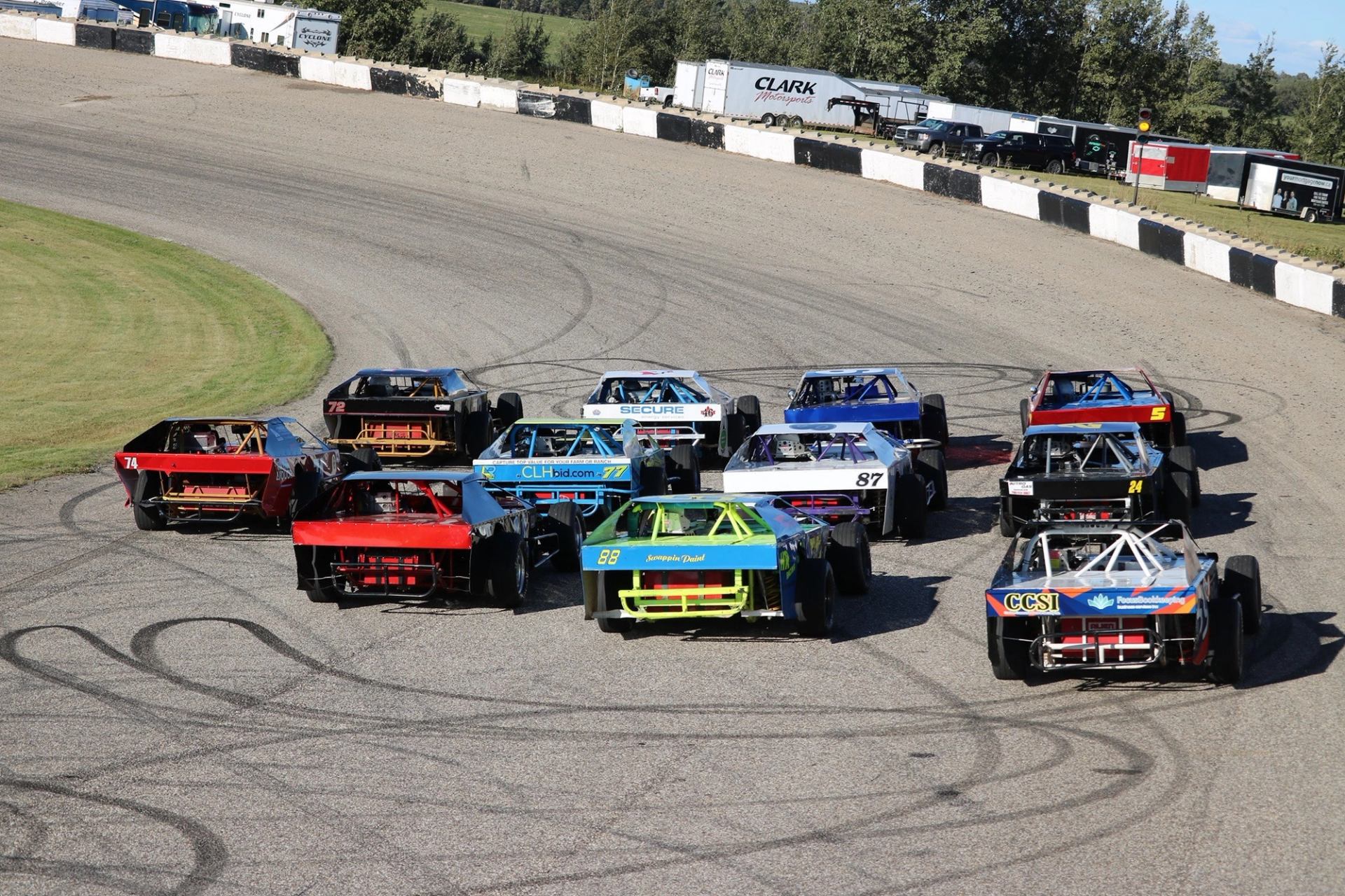 Group of modified race cars driving in formation on a curved section of track.