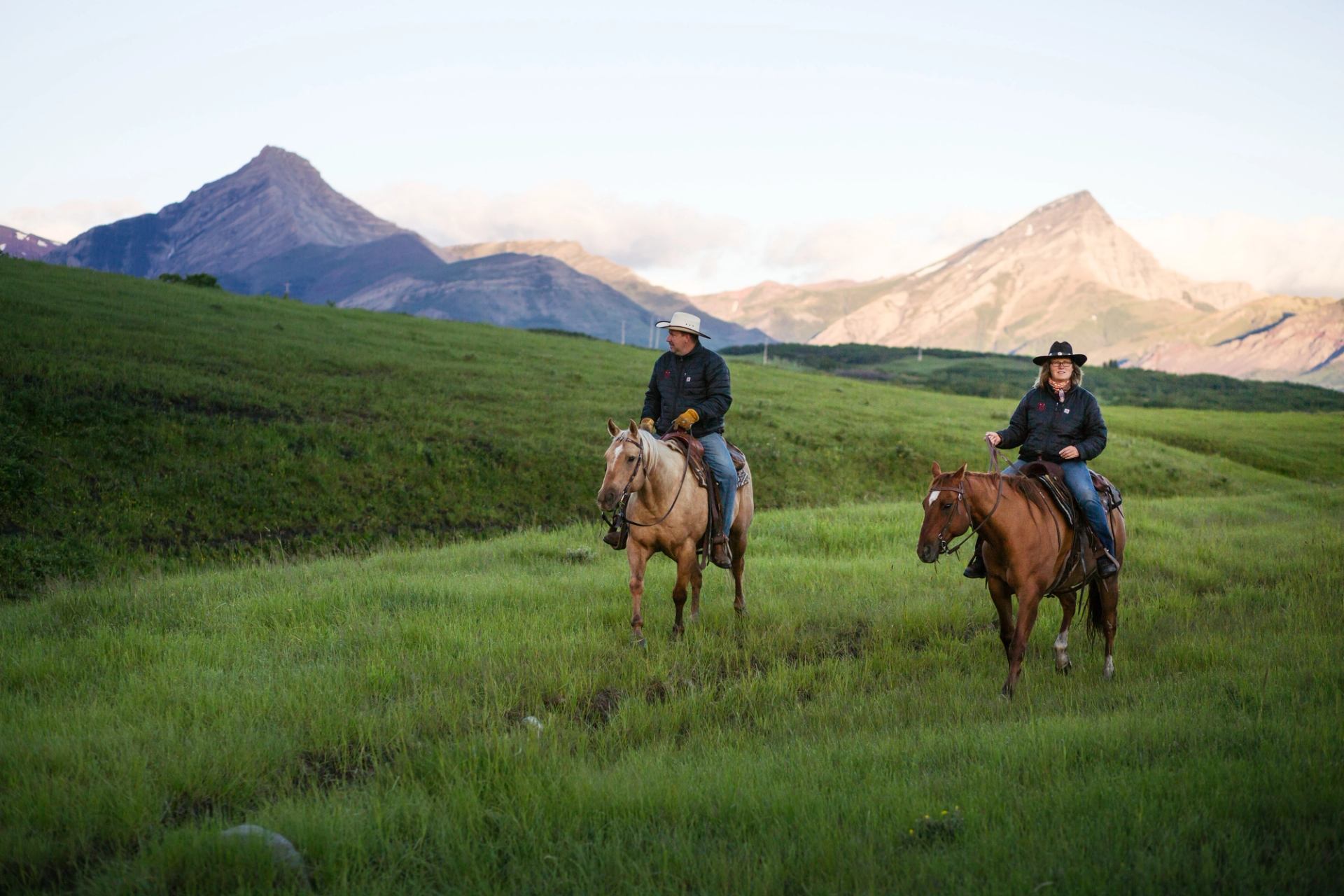 Two people riding horses at sunrise.