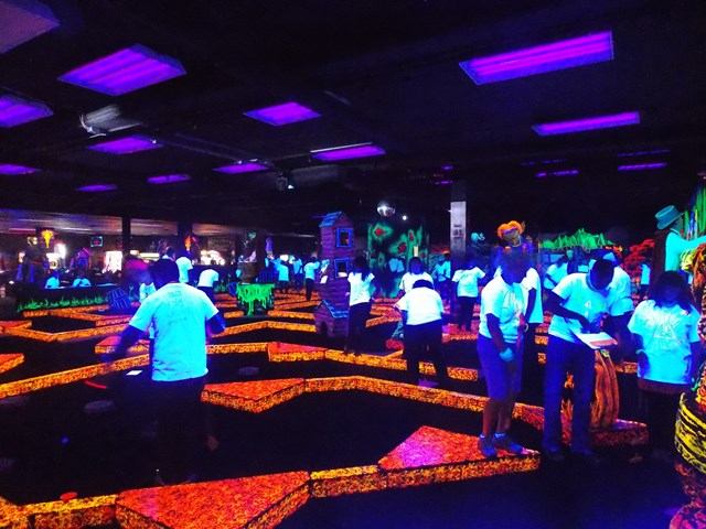 Neon-lit mini-golf course with players and colorful obstacles in an indoor arcade.