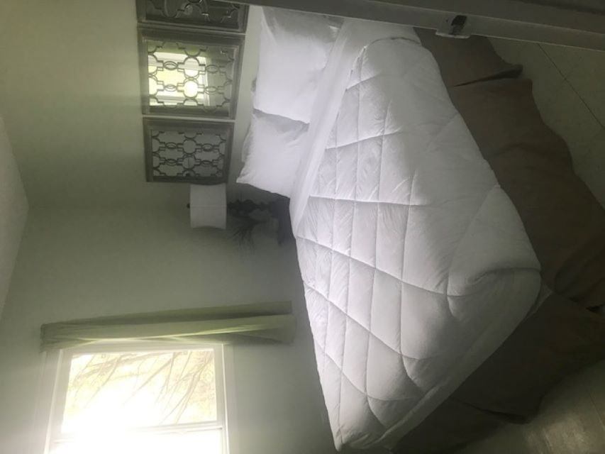 Bed with white quilt, ceiling lamp, and decorative window screen in cabin interior.