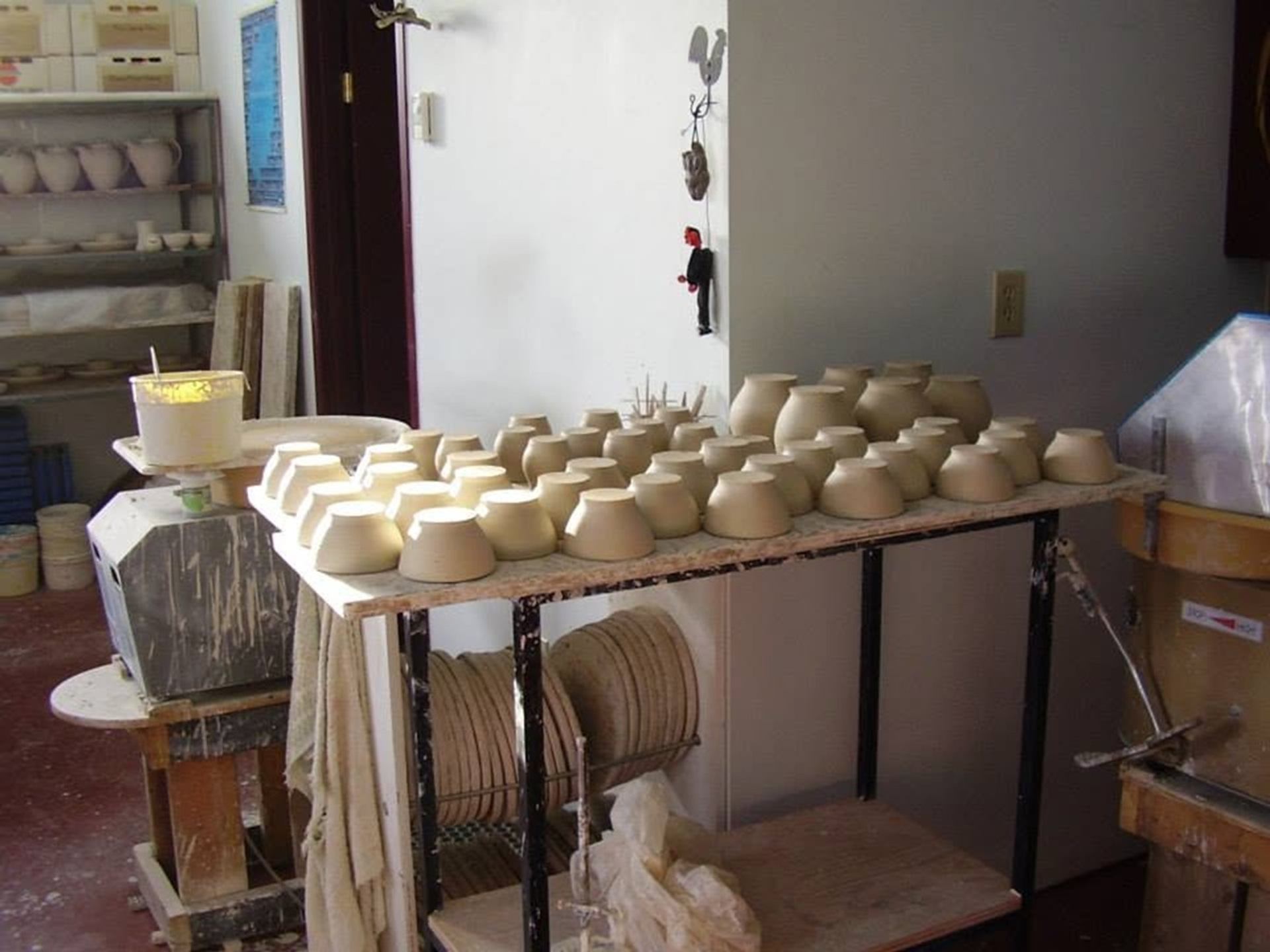 Freshly formed clay bowls and pottery pieces rest on shelves inside a working ceramics studio.
