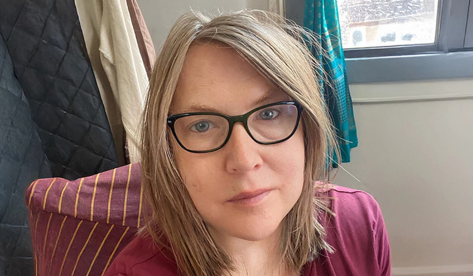 Person wearing glasses seated indoors near a window, with hanging fabrics in background. Provide your feedback on BizChat