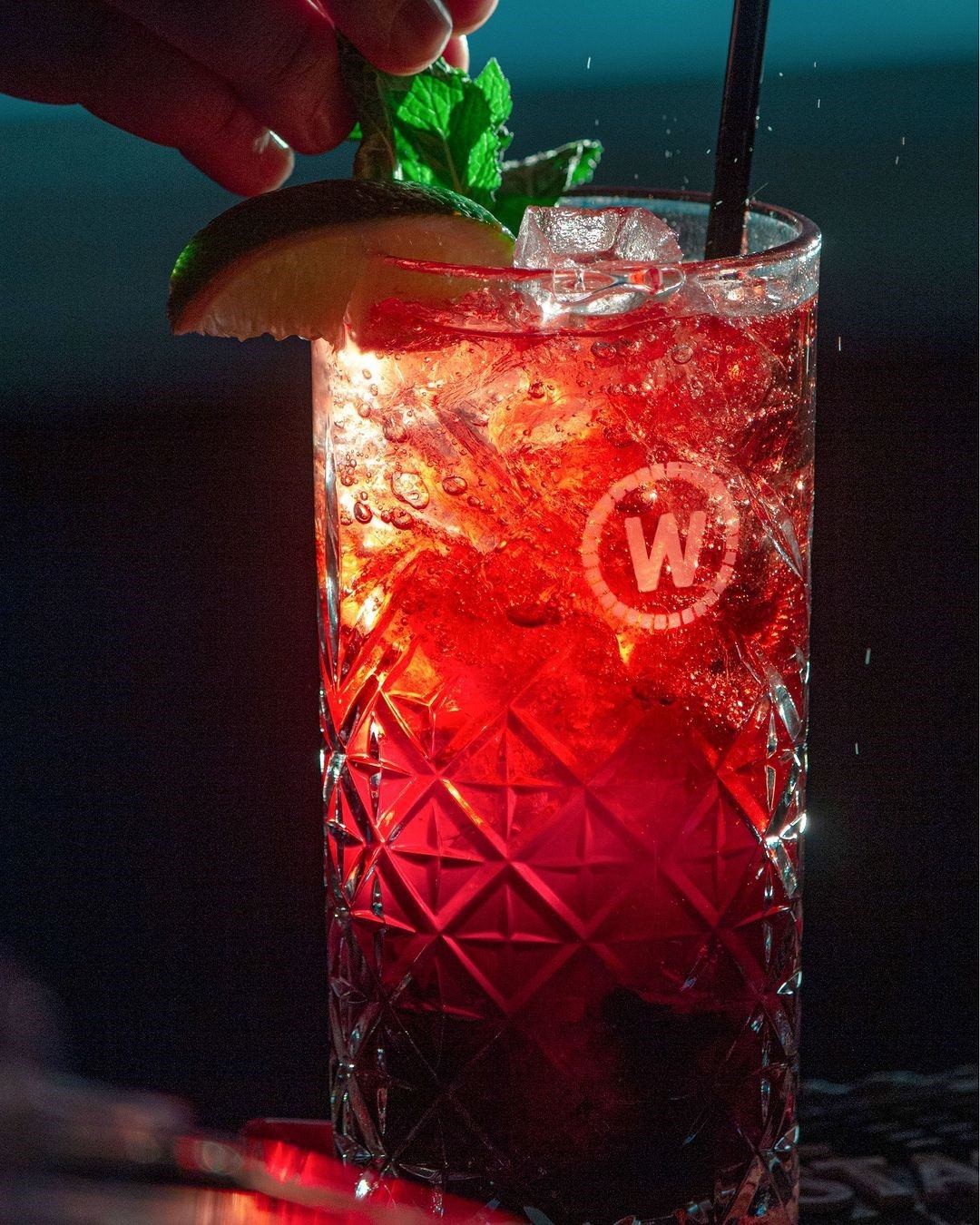 A tall crystal glass filled with a glowing red cocktail over ice.