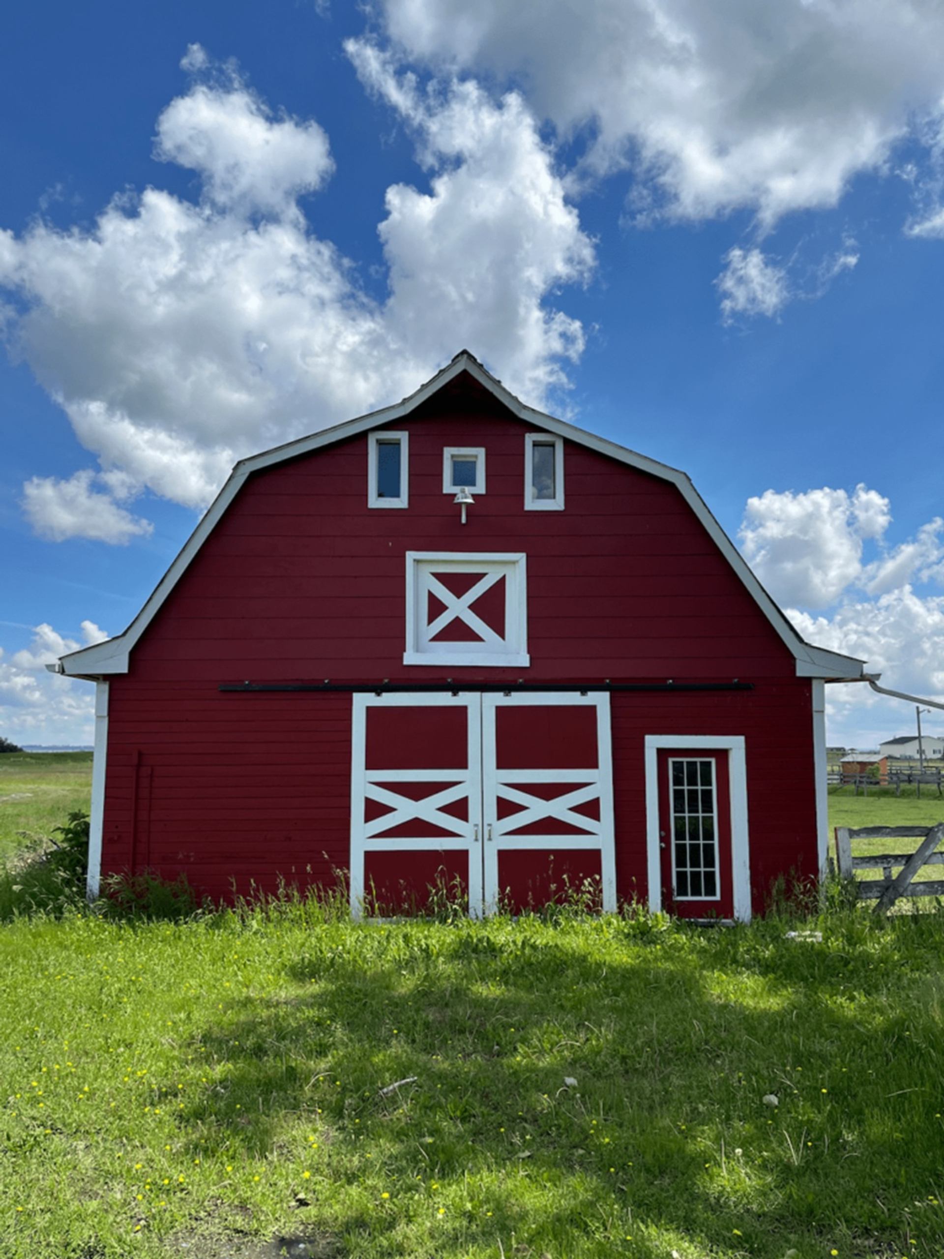 Red barn with white trim stands in grassy field under blue sky with clouds.
