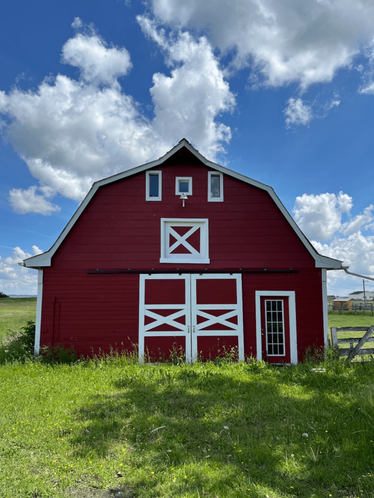 Red barn with white trim stands in grassy field under blue sky with clouds.