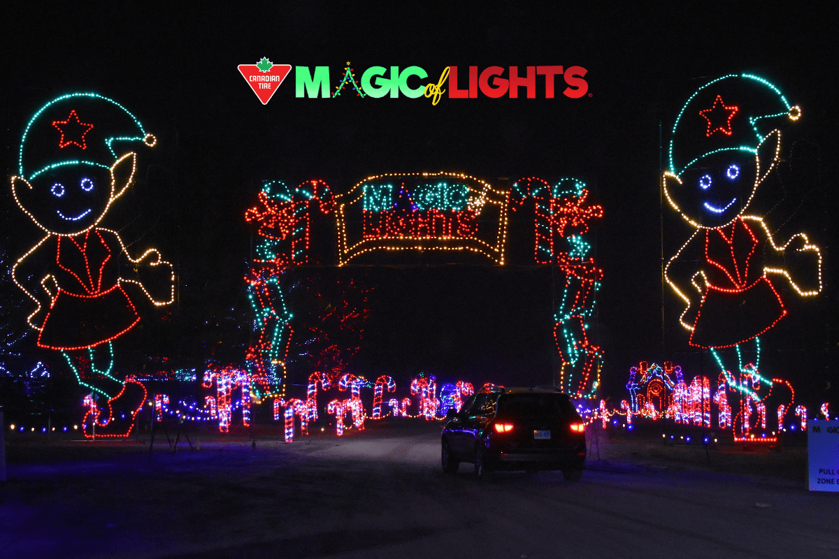 Car driving through Magic of Lights holiday display with giant elf decorations.