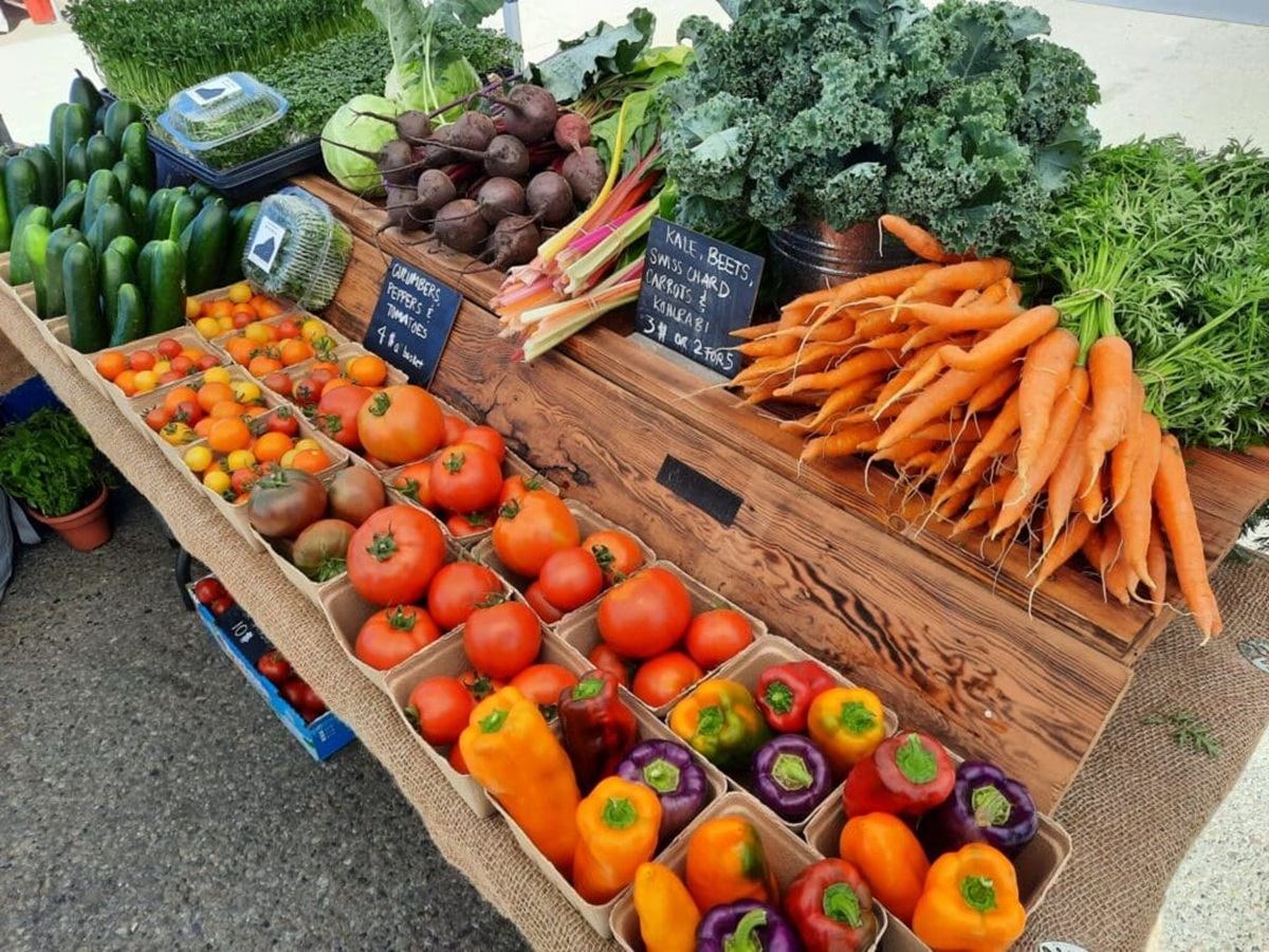 Farmers’ market stall with tomatoes, carrots, peppers, cucumbers, kale and beets displayed.