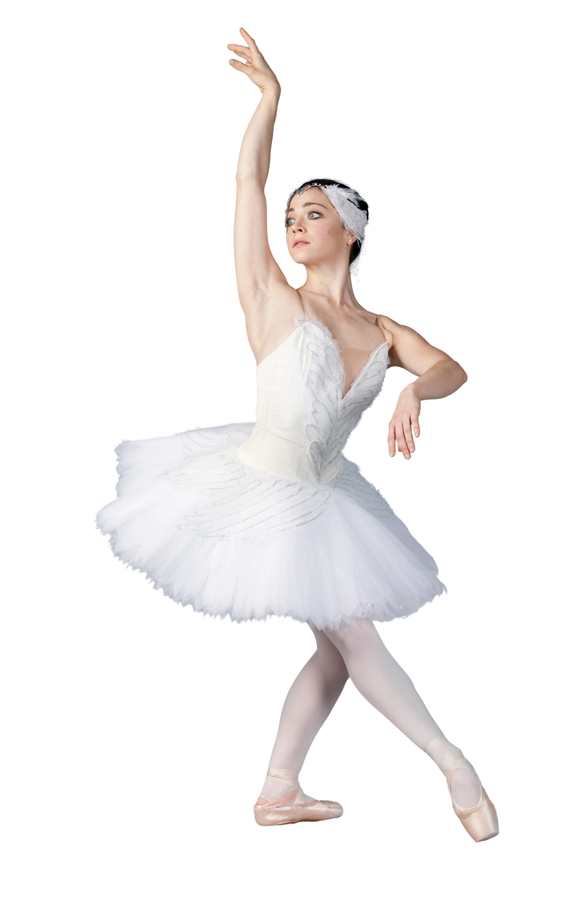 Ballet dancer in white tutu and feathered headpiece poses en pointe against black background.