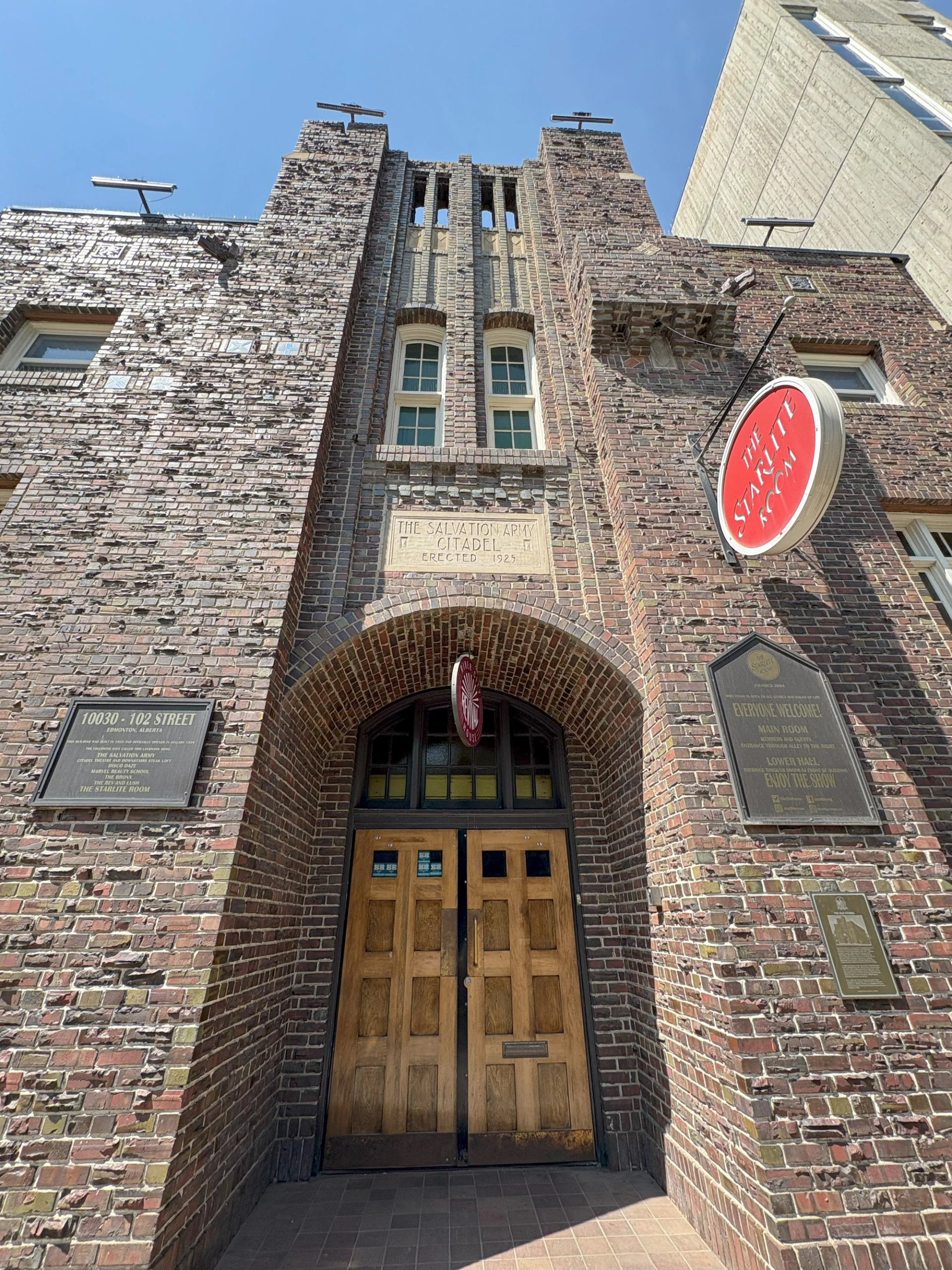 Brick building entrance with wooden doors, plaques, and a red circular sign at Edmonton Citadel.