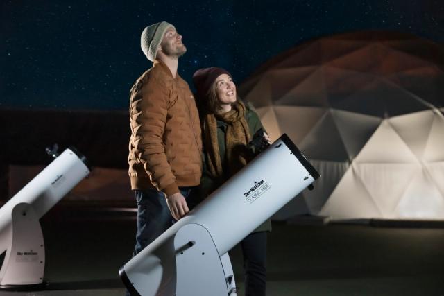 Young couple outside looking skyward, telescopes on ground.