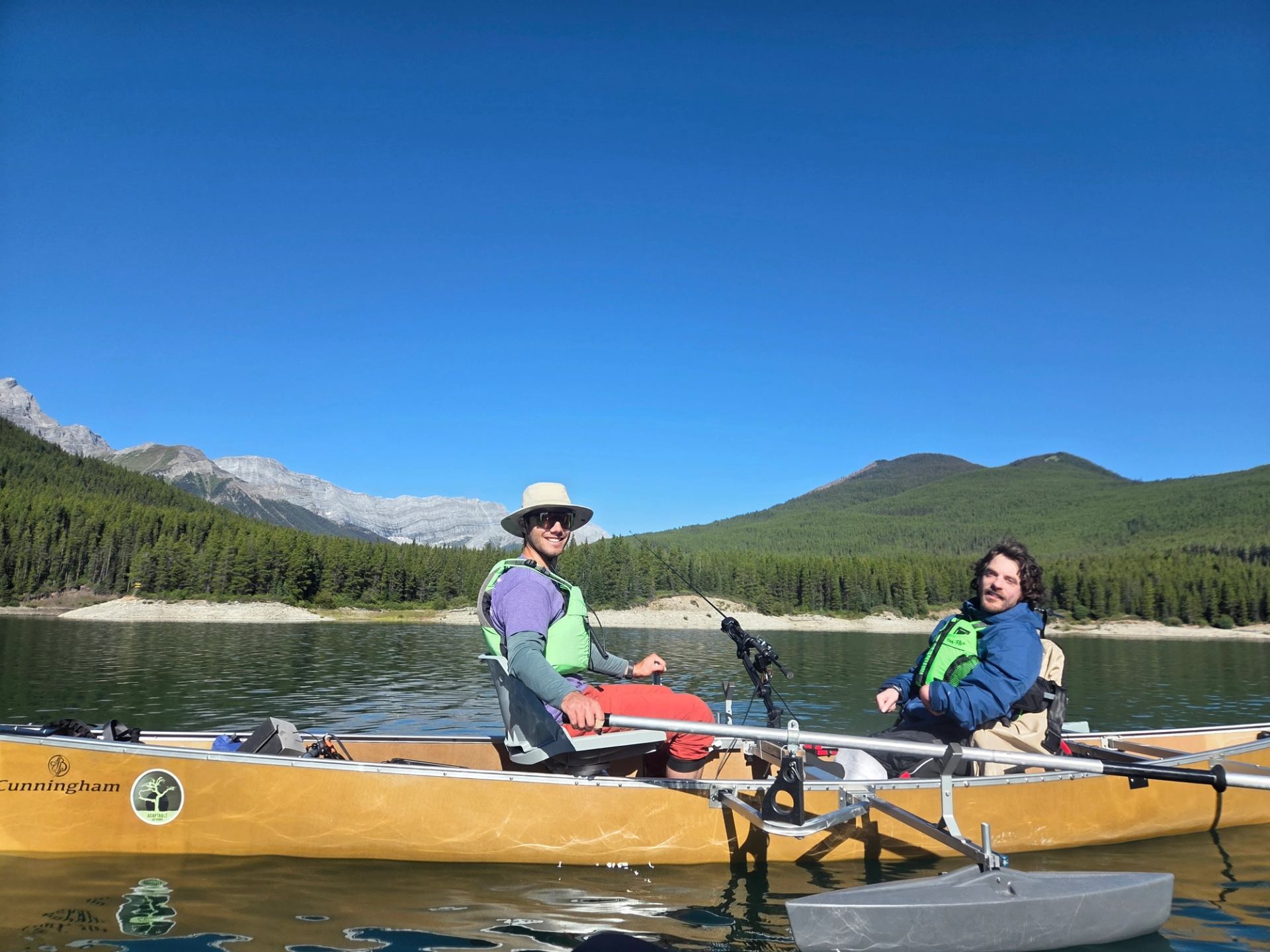 Two people kayaking on a clear lake with mountains and forest in the background.